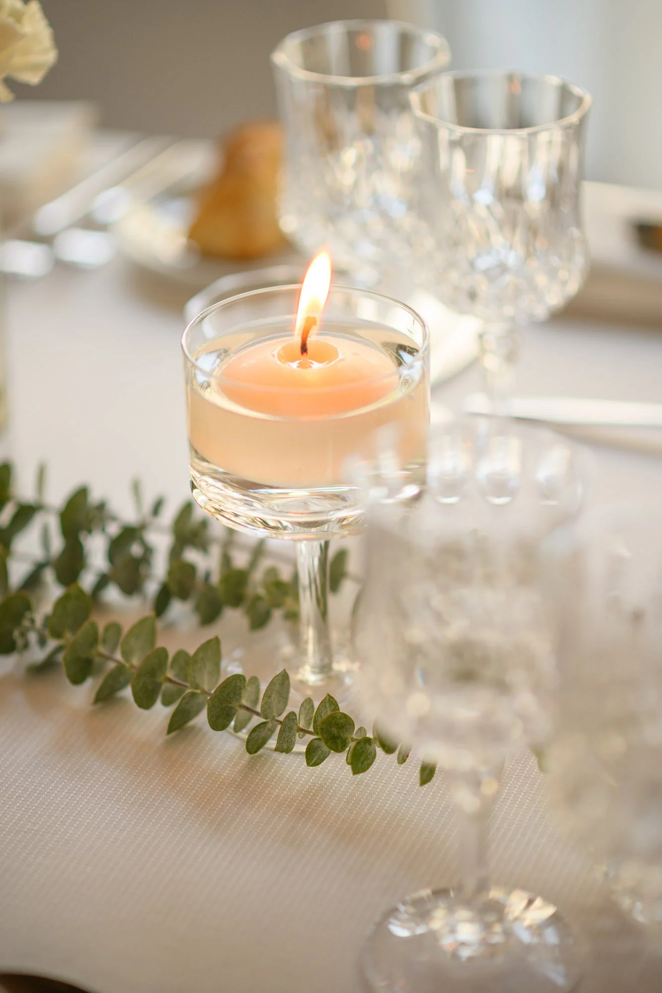 Bougie allumée sur une table élégante avec des verres en cristal et des décorations végétales.