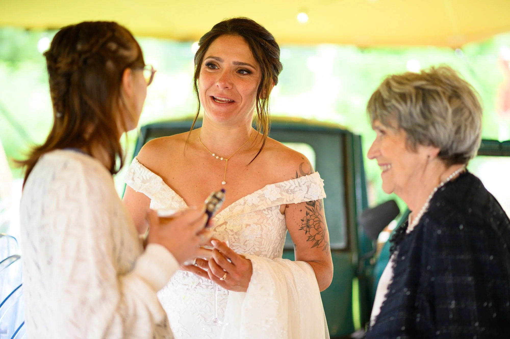 Trois femmes souriantes en conversation lors d'un événement en plein air, avec un fond flou de nature.