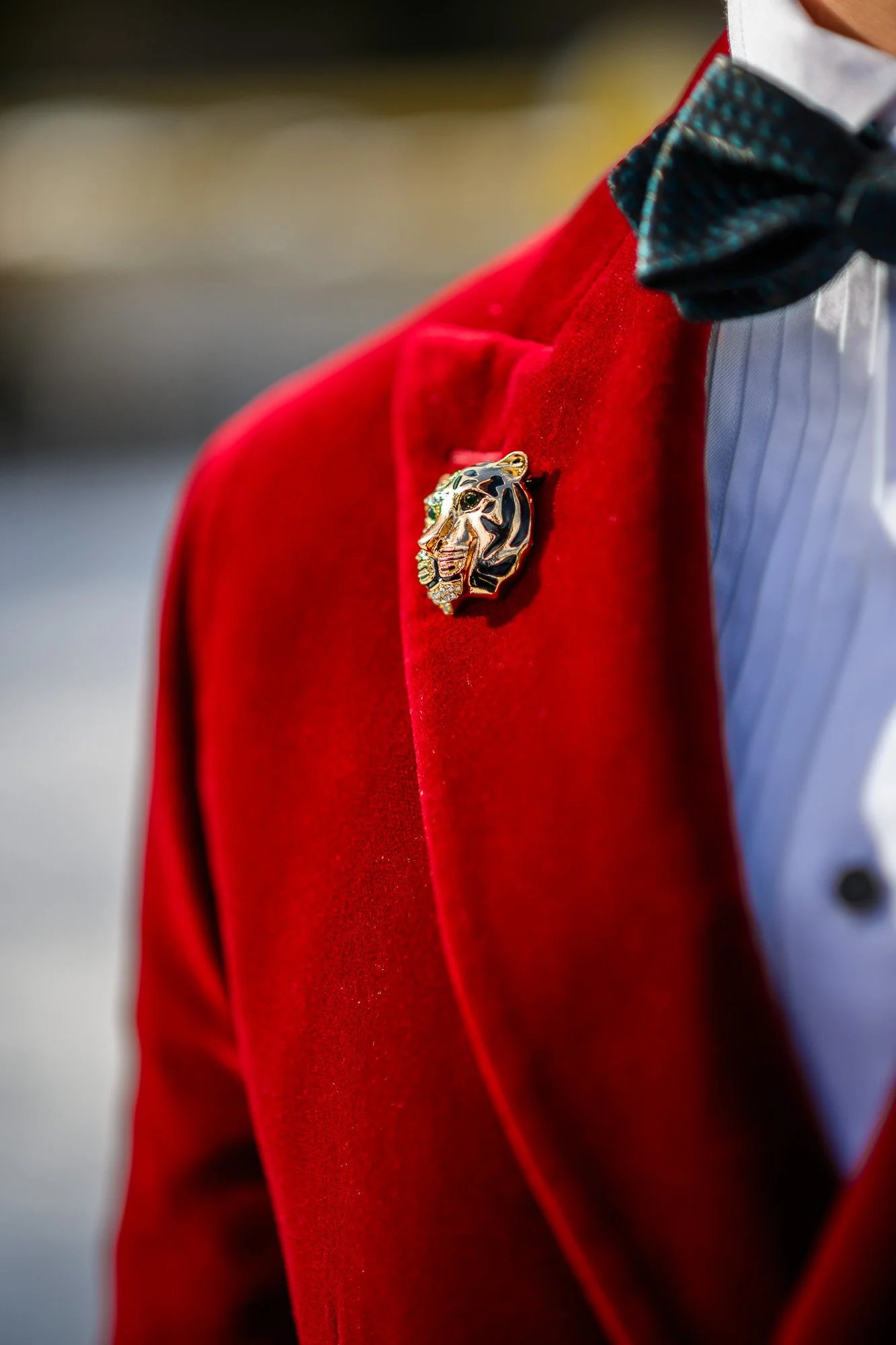 Un homme porte une veste rouge, une chemise blanche et un nœud papillon noir avec des pois blancs, avec une broche en forme de tête de tigre en or sertie de pierres précieuses.