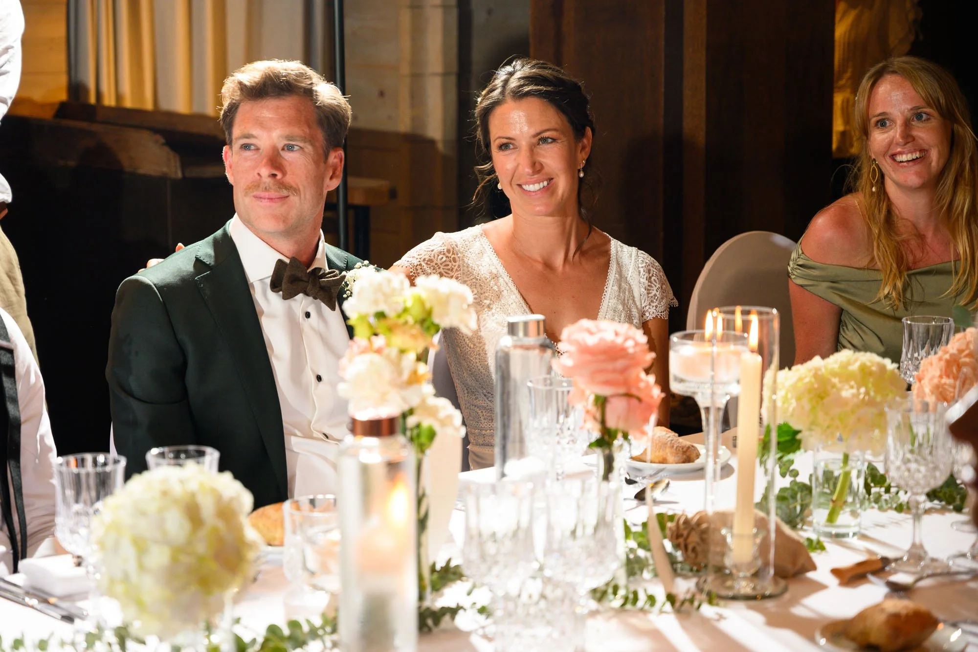 Groupe de personnes souriantes assises à une table lors d'une célébration, décorée de fleurs et de bougies.