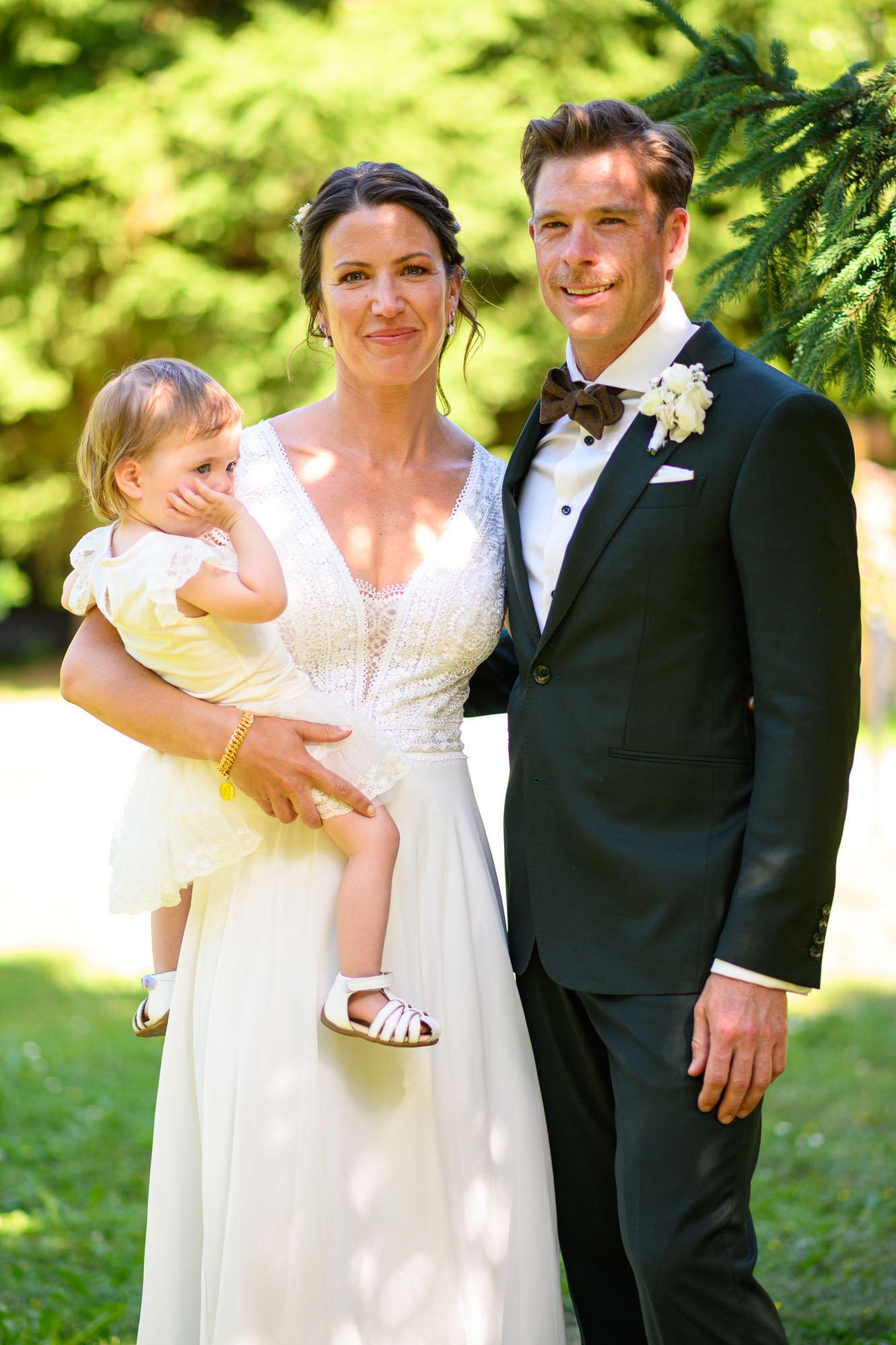 Un couple en mariage pose avec une petite fille dans un parc en plein air