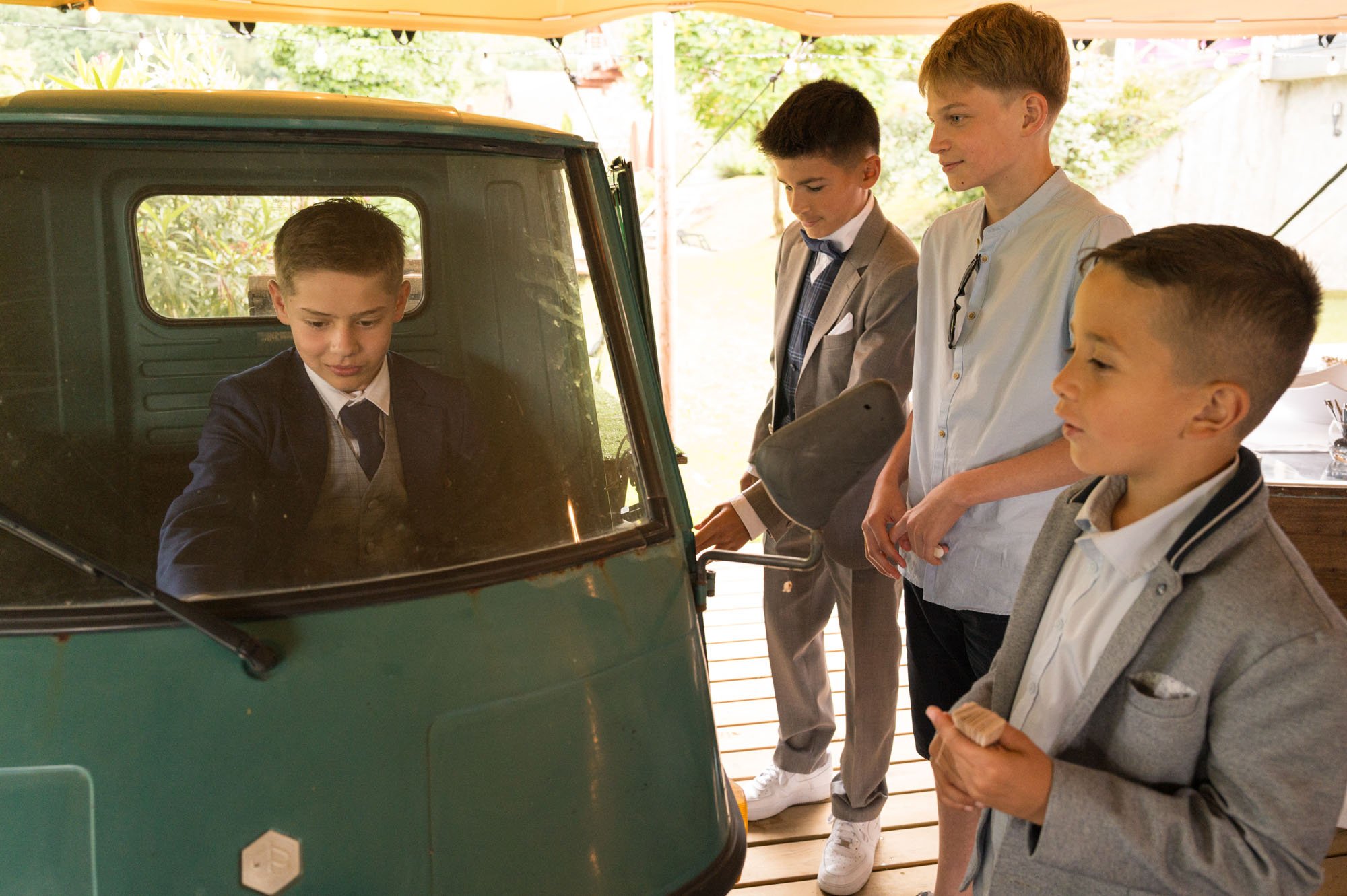 Groupe de garçons en costume regardant une petite voiture vintage.