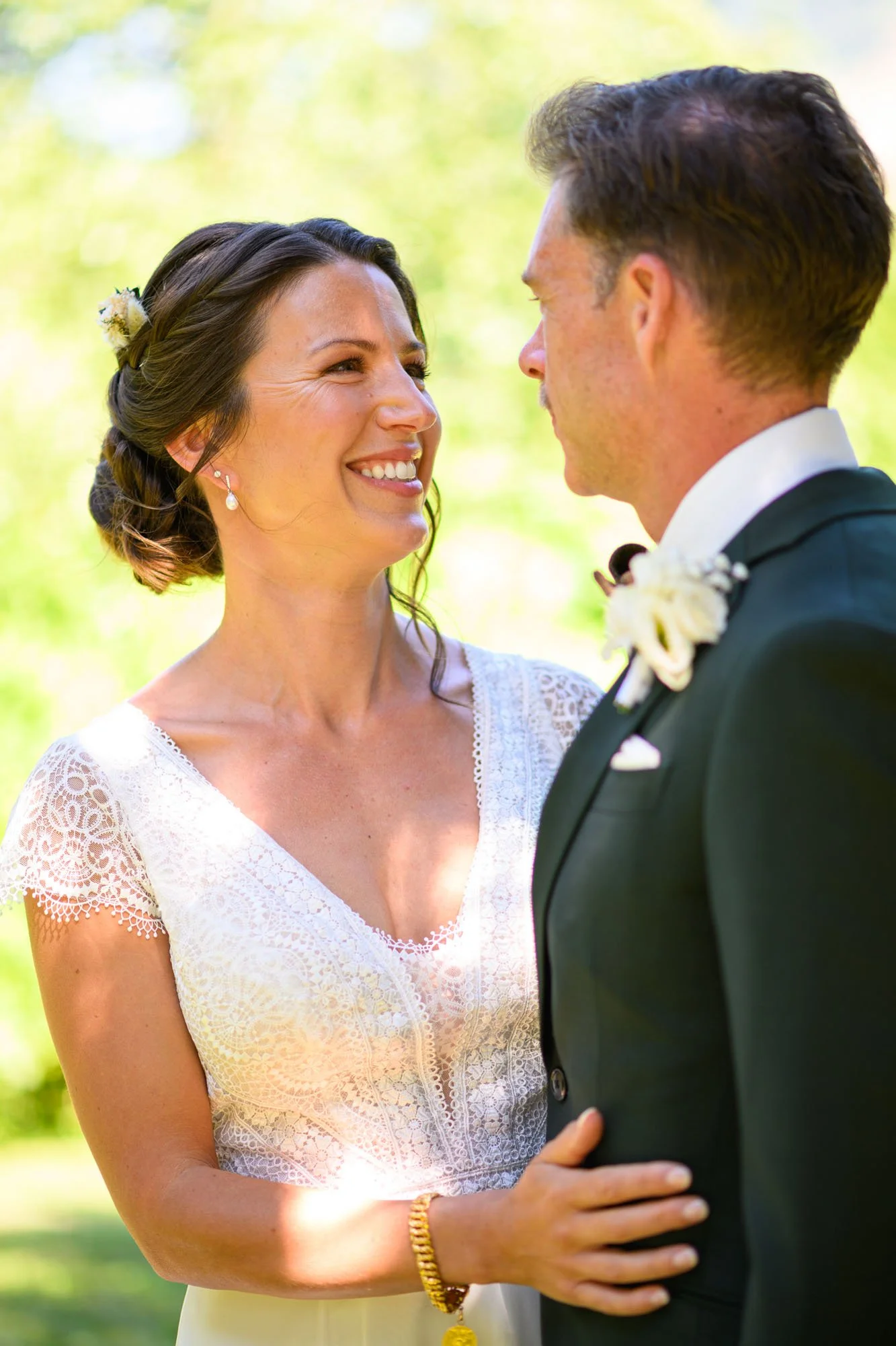 Un couple de mariés souriant lors de leur mariage en plein air avec un fond de verdure.