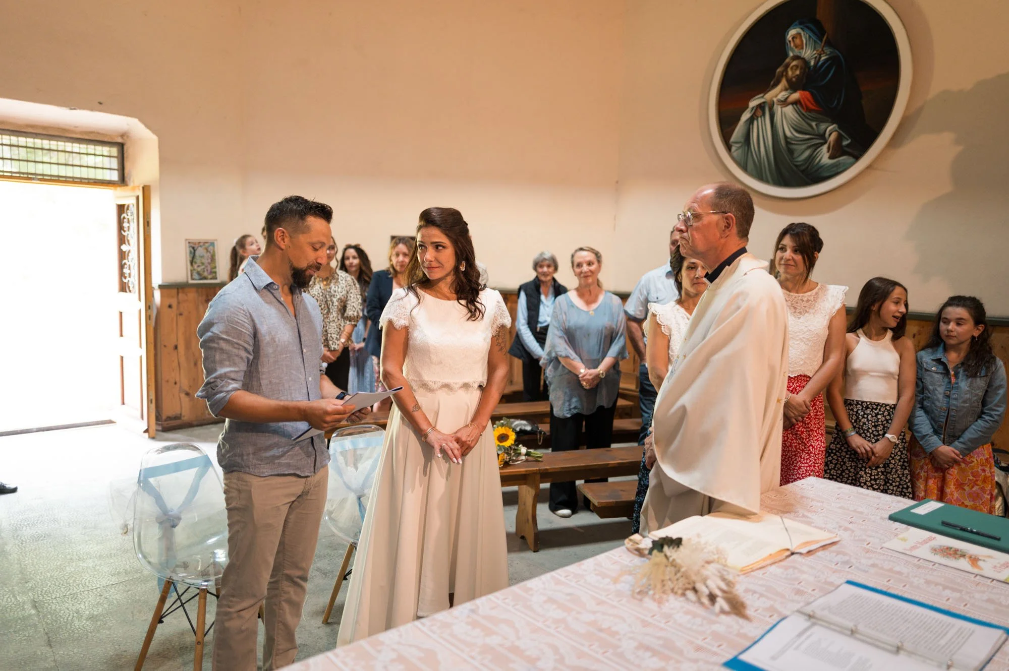 Un couple échange leurs vœux lors d'une cérémonie de mariage religieuse dans une église, avec des invités en arrière-plan.