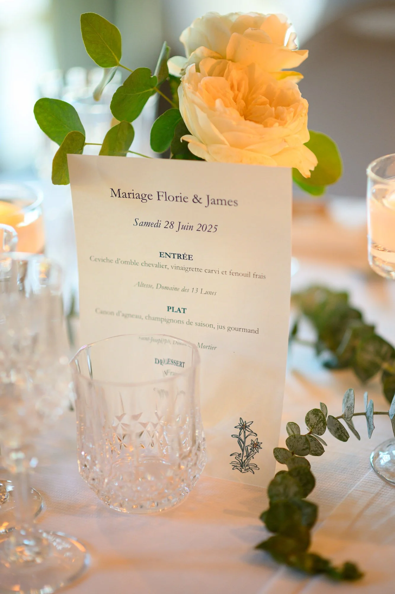Menu de mariage sur une table avec des fleurs blanches et des verres en cristal.