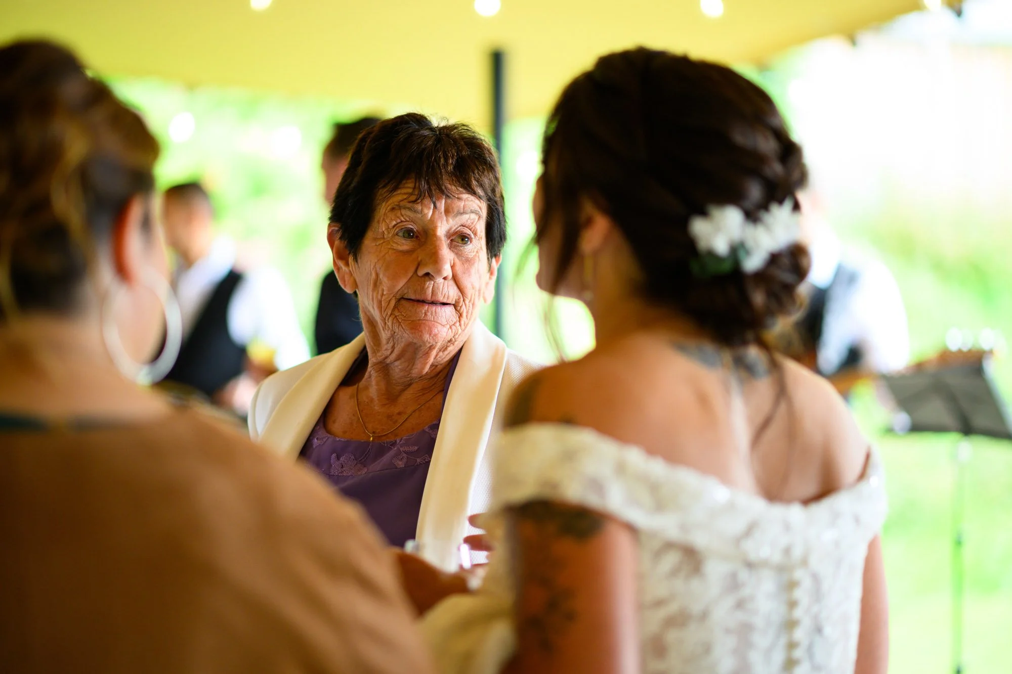 Une grand-mère et une mariée en conversation lors d'un mariage, sous un chapiteau, en arrière-plan un groupe de musiciens.