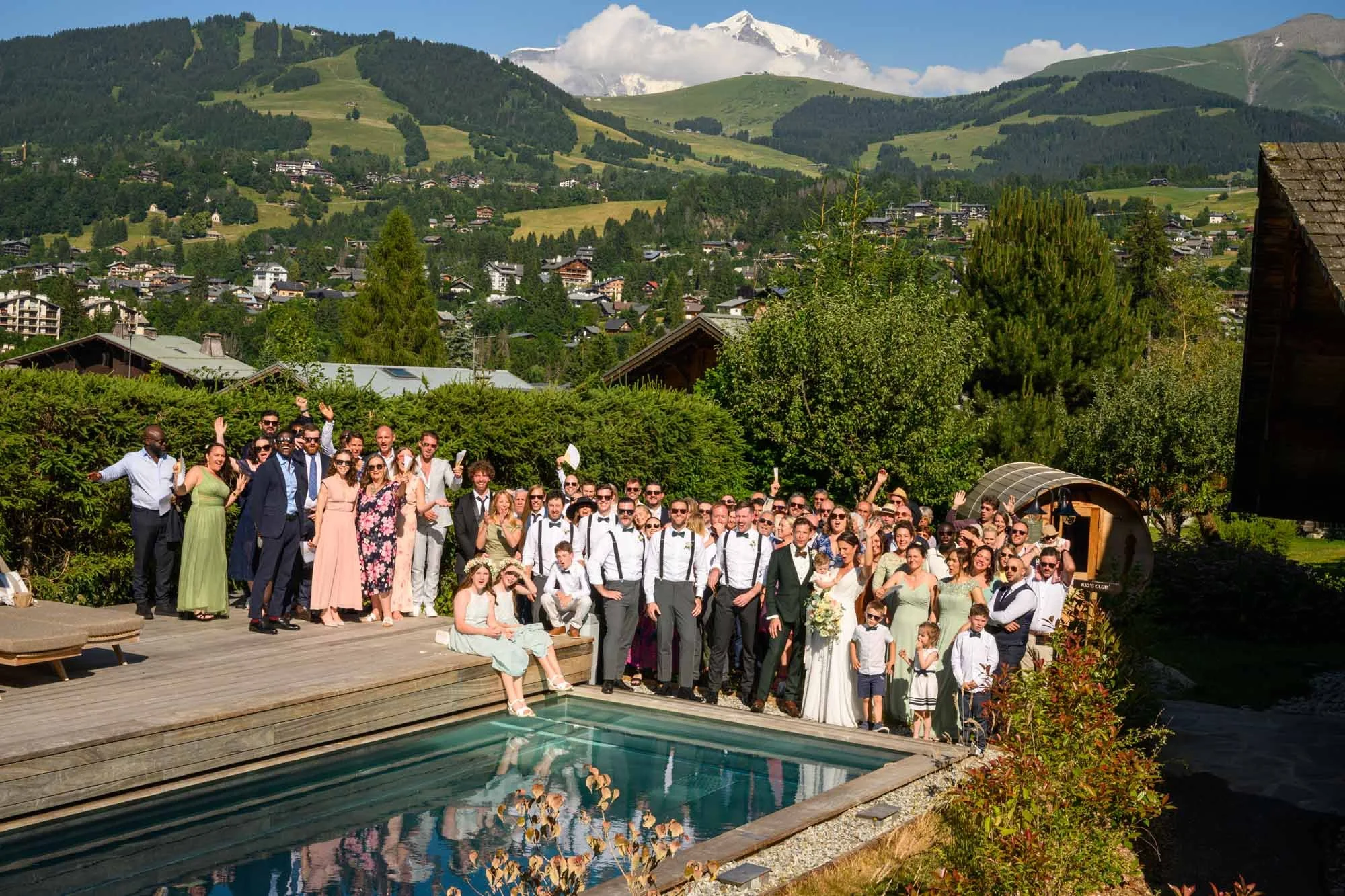 Groupe de personnes lors d'un mariage en plein air, avec montagnes et nature en arrière-plan, autour d'une piscine.