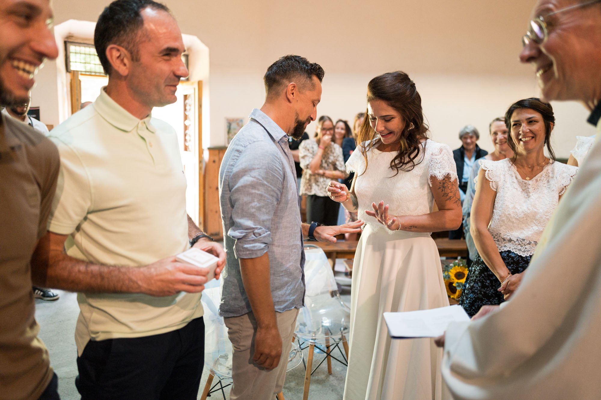 Un couple lors d'une cérémonie de mariage en intérieur, avec des invités qui les entourent.