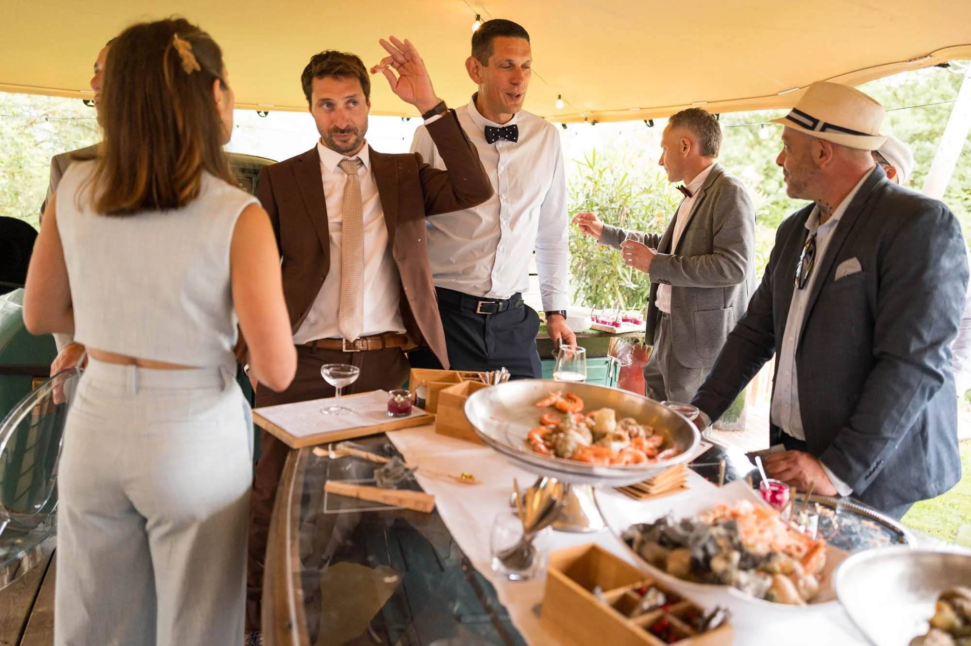 Groupe de personnes en discussion lors d'un événement en plein air, avec un service de nourriture et de boissons sous une tente