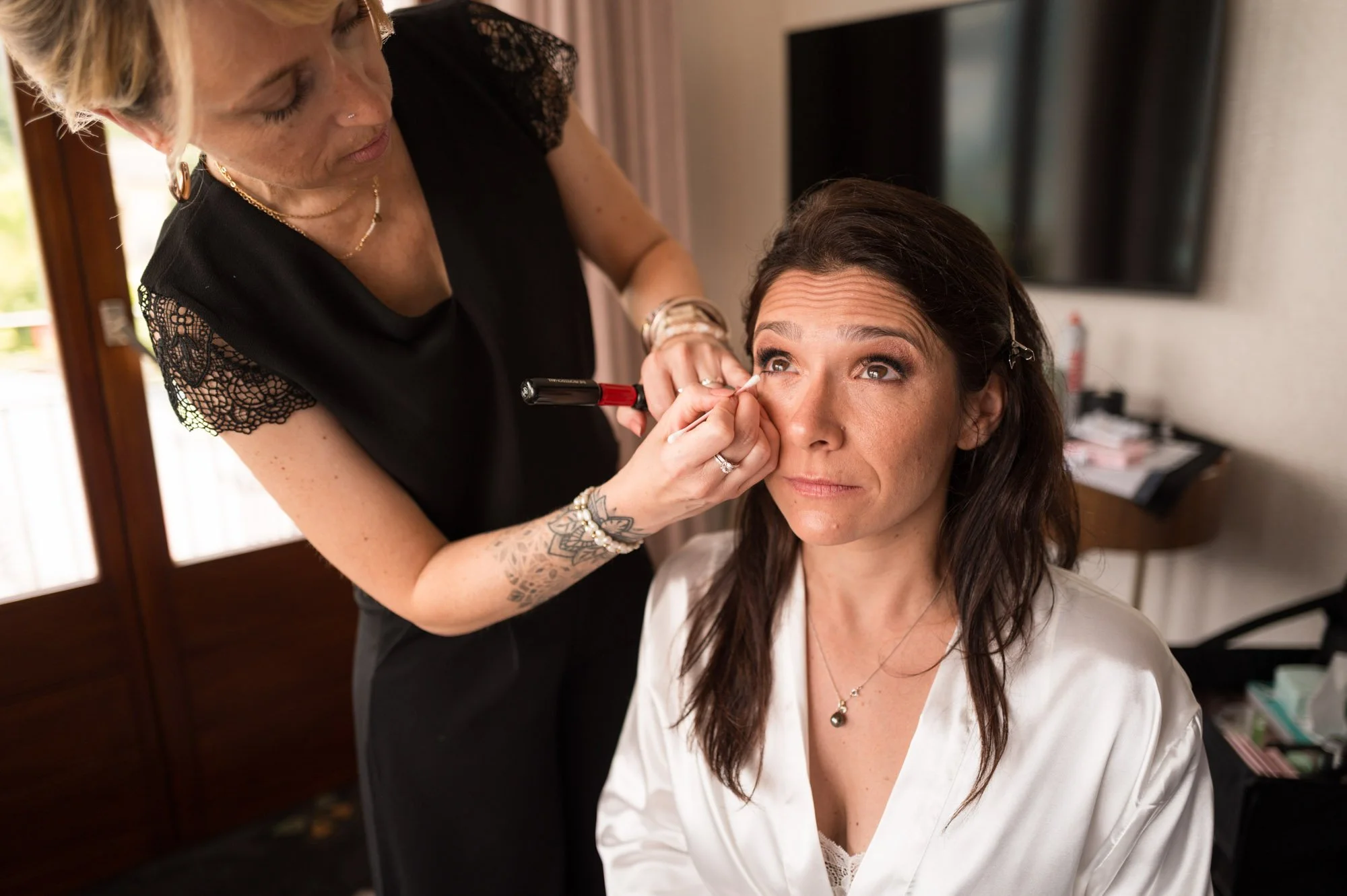 Une femme est en train de se faire maquiller par une autre femme dans une pièce lumineuse.