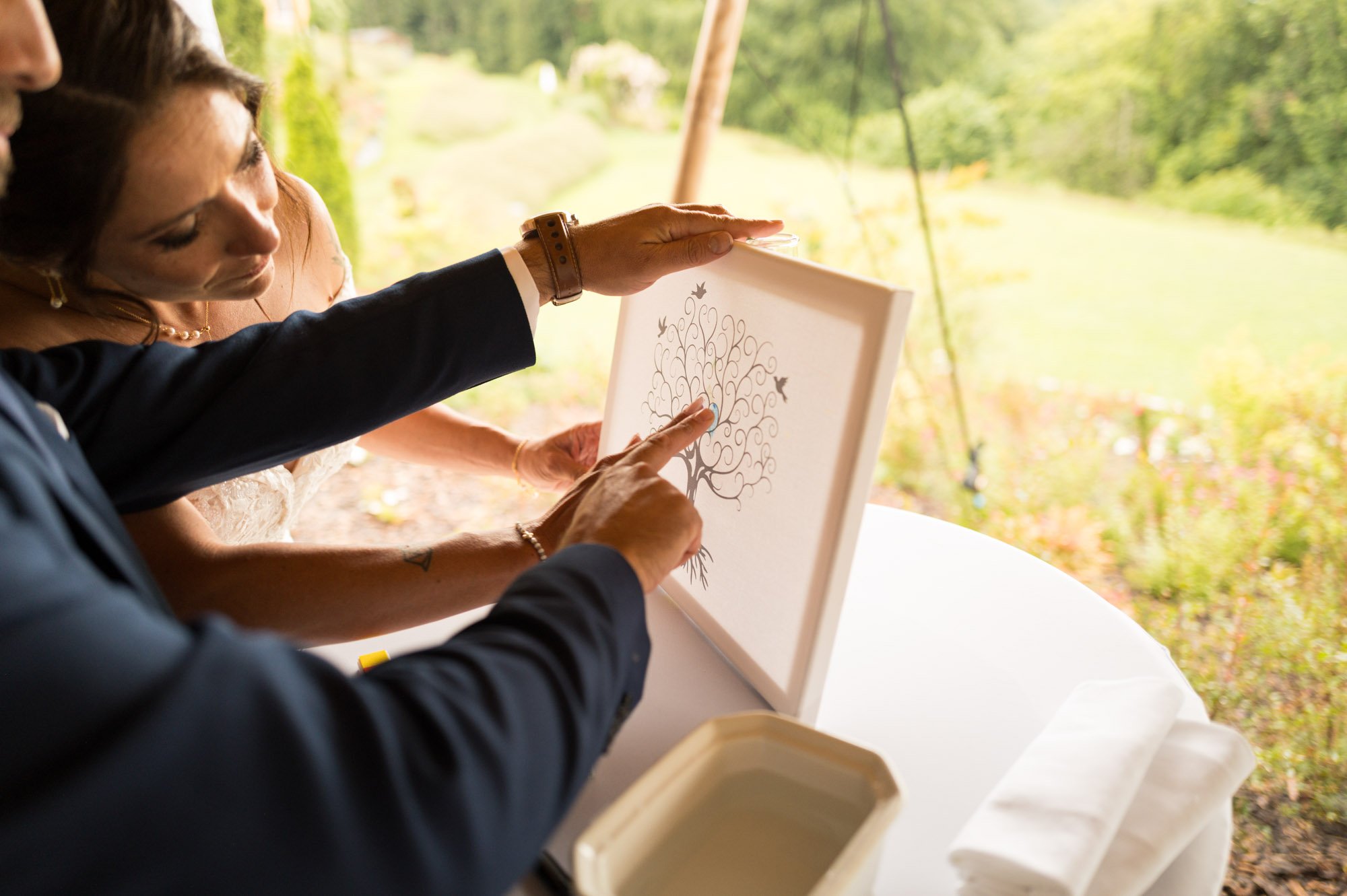 Deux personnes regardant une illustration d'un arbre sur une toile, lors d'une activité en plein air, avec un environnement naturel verdoyant en arrière-plan.