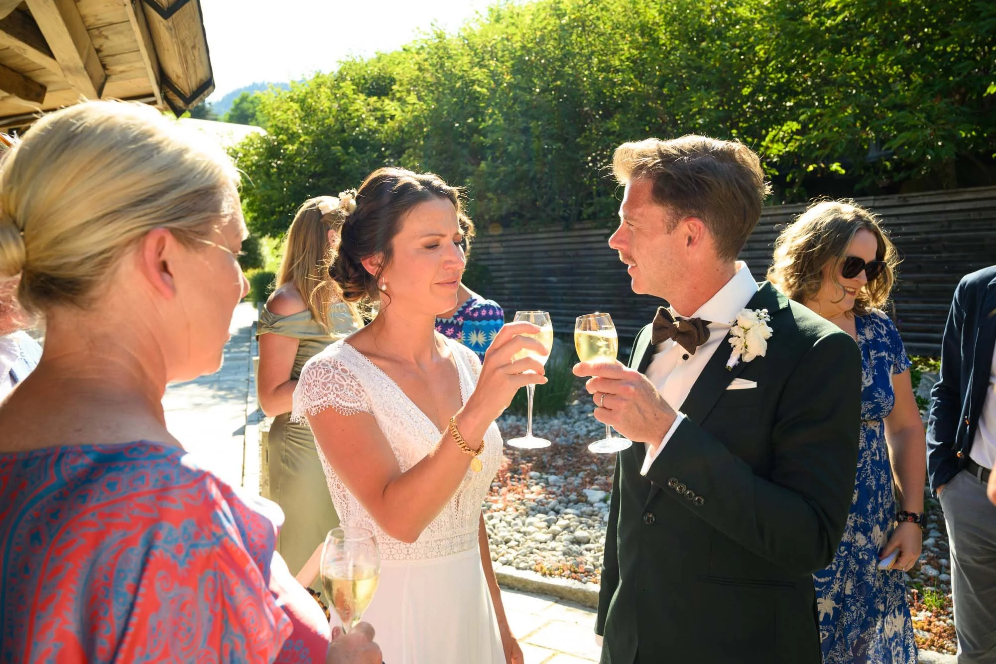 Groupe de personnes lors d'une célébration en plein air, notamment un couple en vêtements de mariage, à un moment de toast avec du champagne.