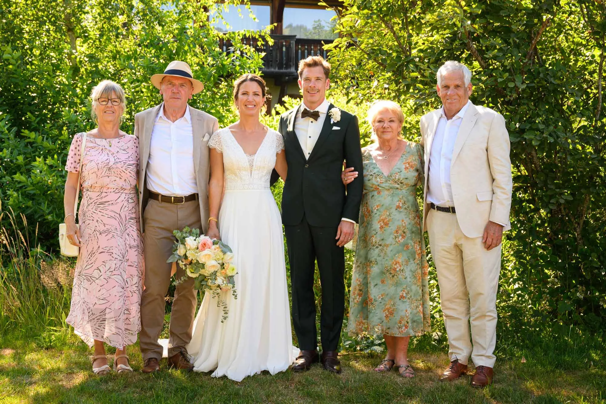 Photo de groupe lors d'un mariage en plein air, avec sept personnes dont un couple de mariés au centre, entourés de membres de leur famille.