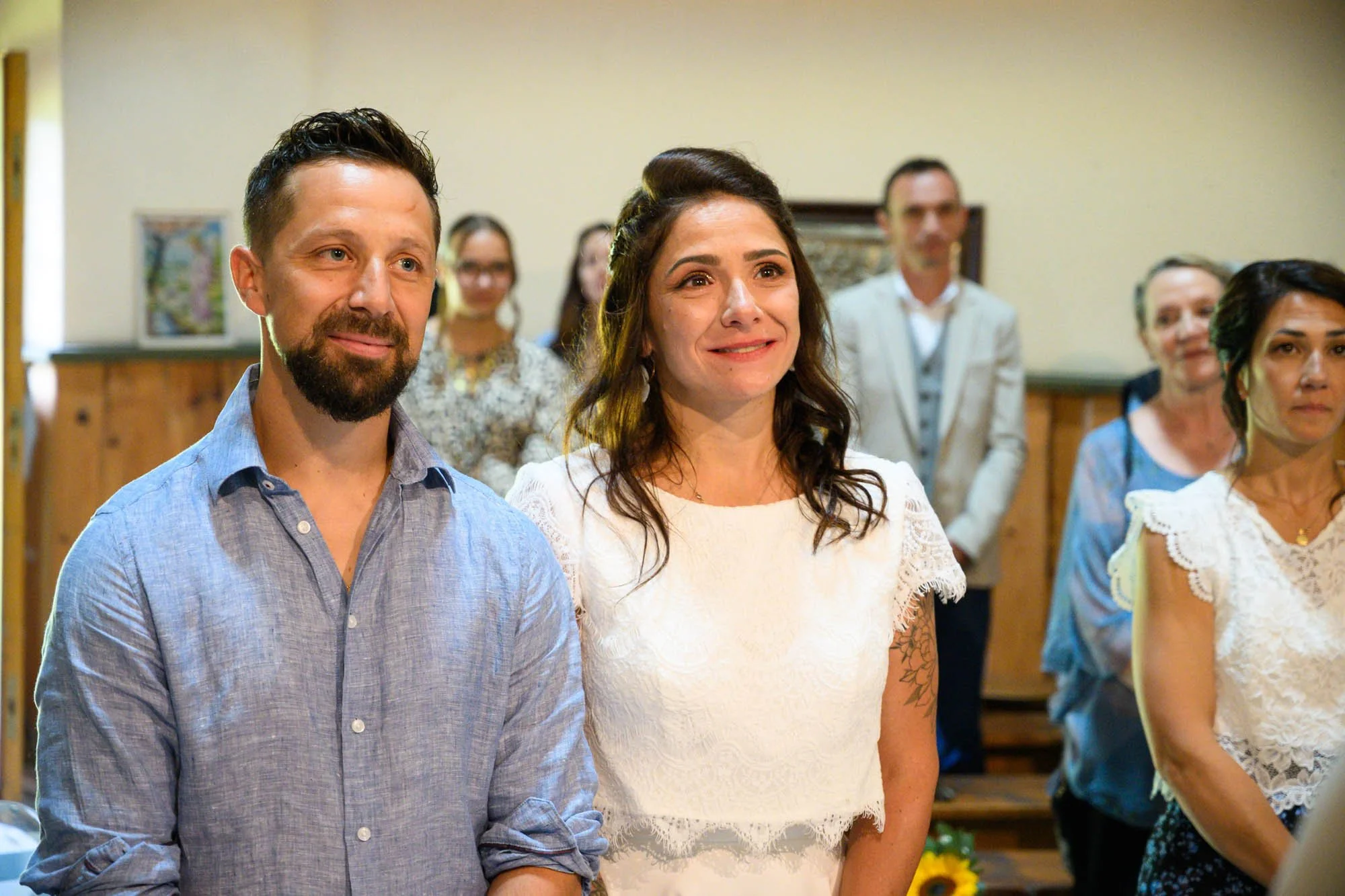 Un couple lors d'une cérémonie, probablement un mariage, entouré d'autres personnes applaudissant et souriant dans une ambiance chaleureuse.