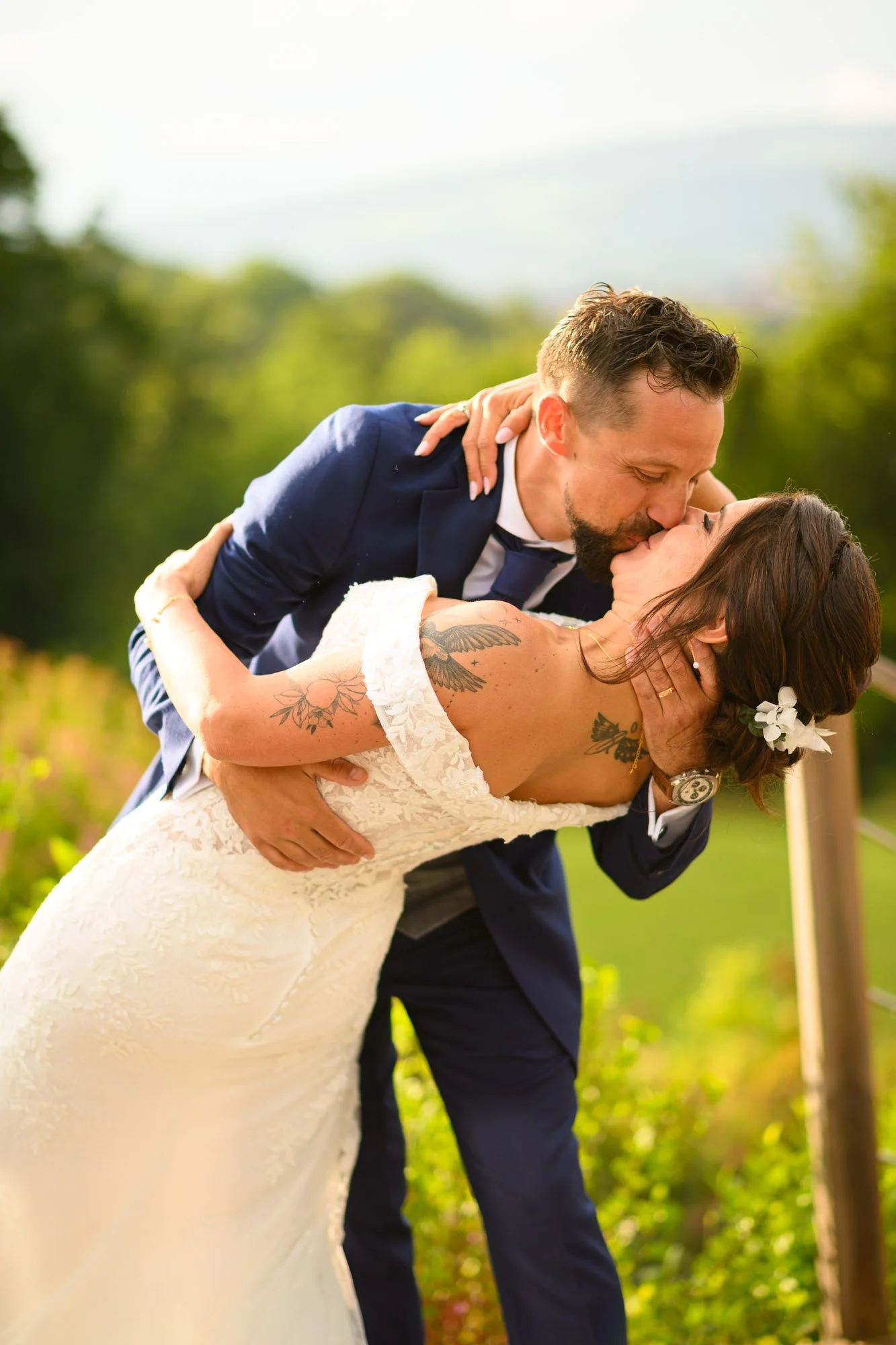 Un couple se embrasse et s'embrasse lors d'une séance photo de mariage en plein air, avec un arrière-plan de nature verdoyante.