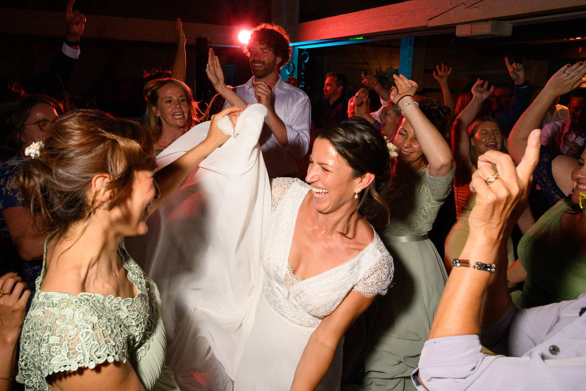 Célébration joyeuse avec des personnes dansant lors d'un mariage, avec une femme en robe blanche et d'autres en vêtements de fête, ambiance festive et dynamique.