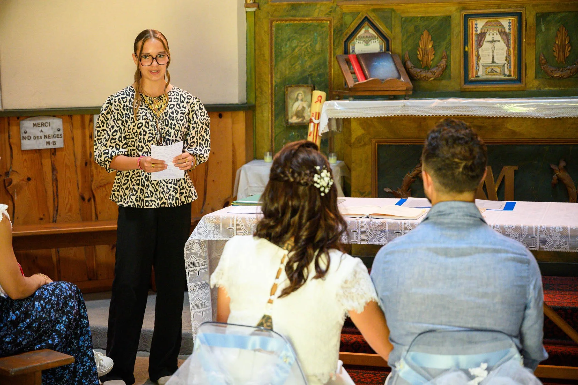 Une femme parle devant un petit groupe dans une pièce decorée avec une ambiance religieuse, un autel et des images religieuses au fond.