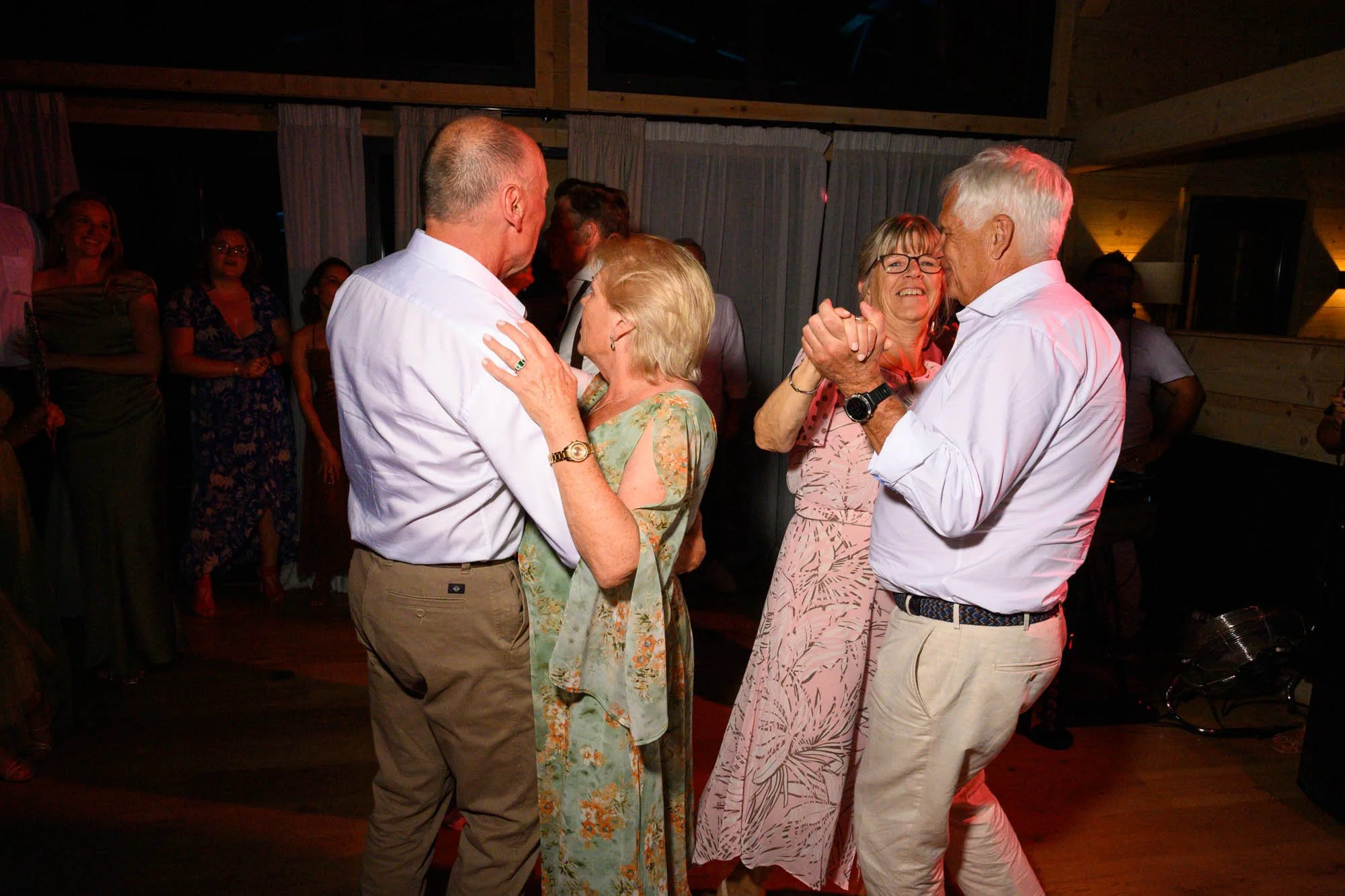 Deux couples dansent et sourient lors d'une fête en intérieur, ambiance chaleureuse et conviviale.