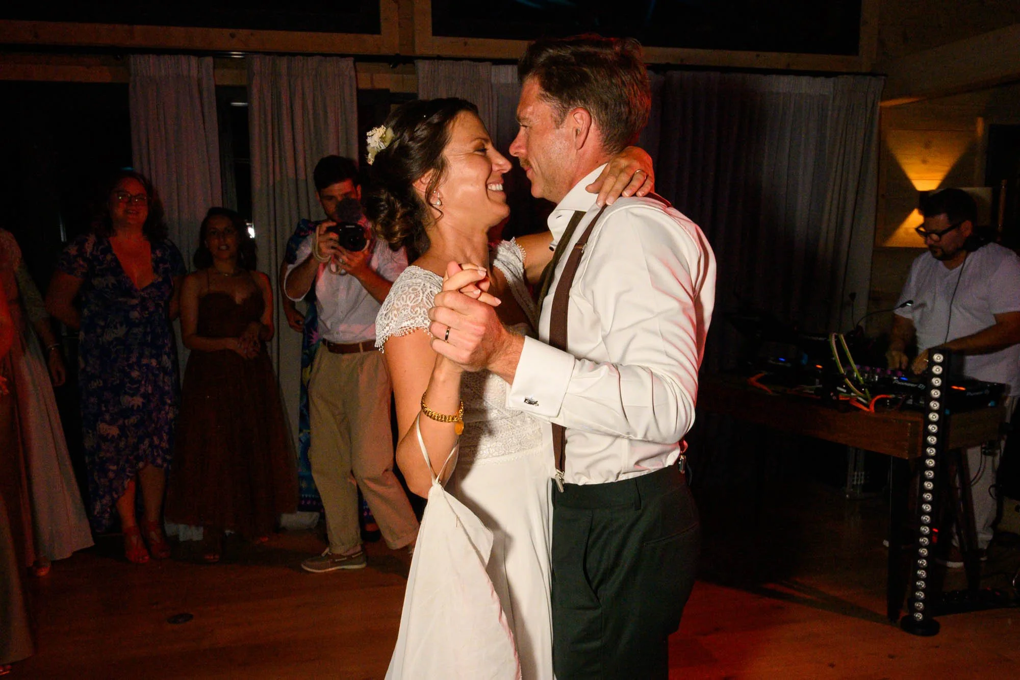 Un couple danse lors d'un mariage, entouré d'invités attentifs, dans une salle avec éclairage tamisé.