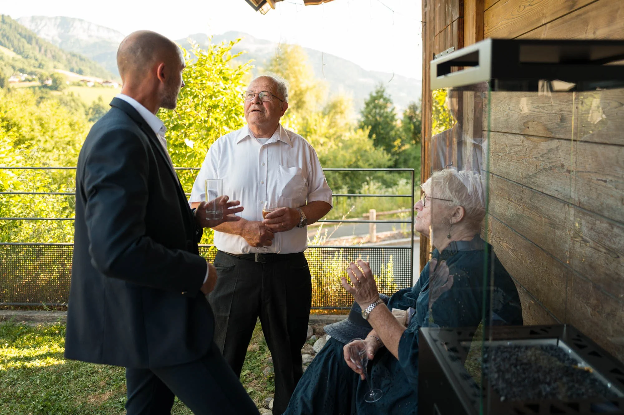 Quatre personnes discutent et tiennent des verres de vin lors d'une réunion à l'extérieur avec un paysage verdoyant en arrière-plan.