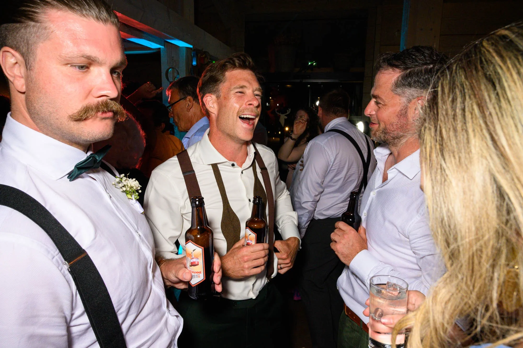 Groupe de personnes souriantes portant des vêtements formels, tenant des bouteilles de bière lors d'une fête ou d'une réception