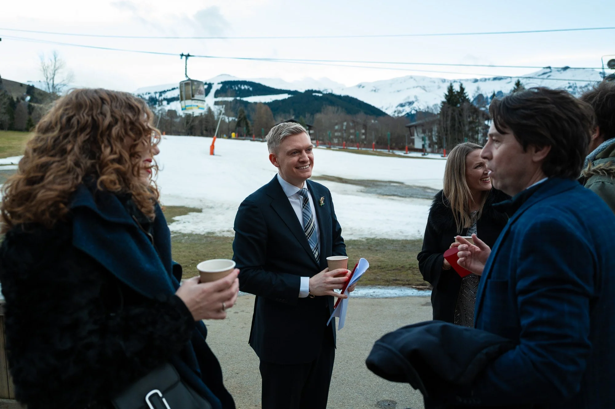 Groupe de personnes discutant en plein air, avec une station de ski enneigée en arrière-plan.