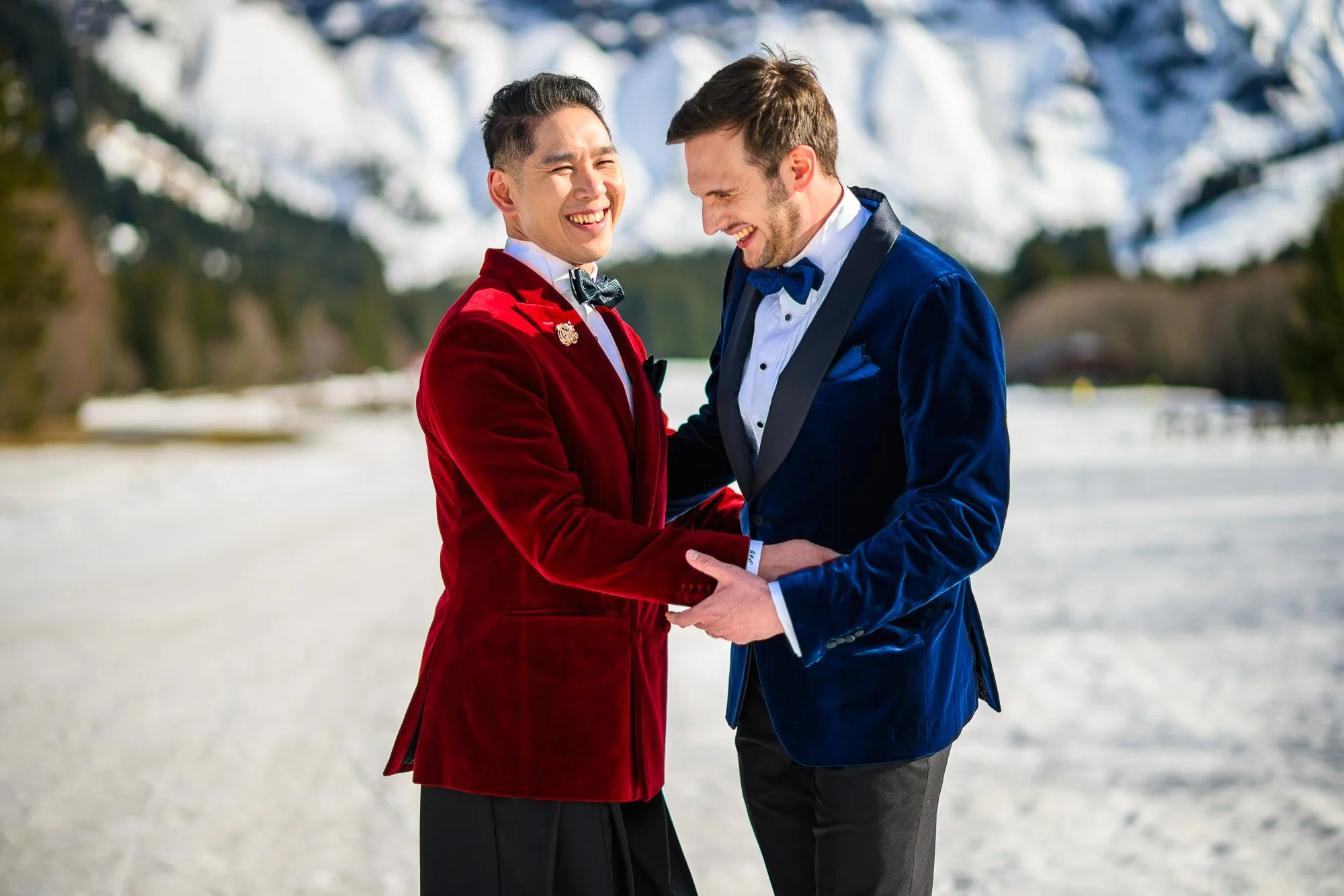 Deux hommes habillés en costumes formels dans un paysage enneigé, souriants et se tenant la main.