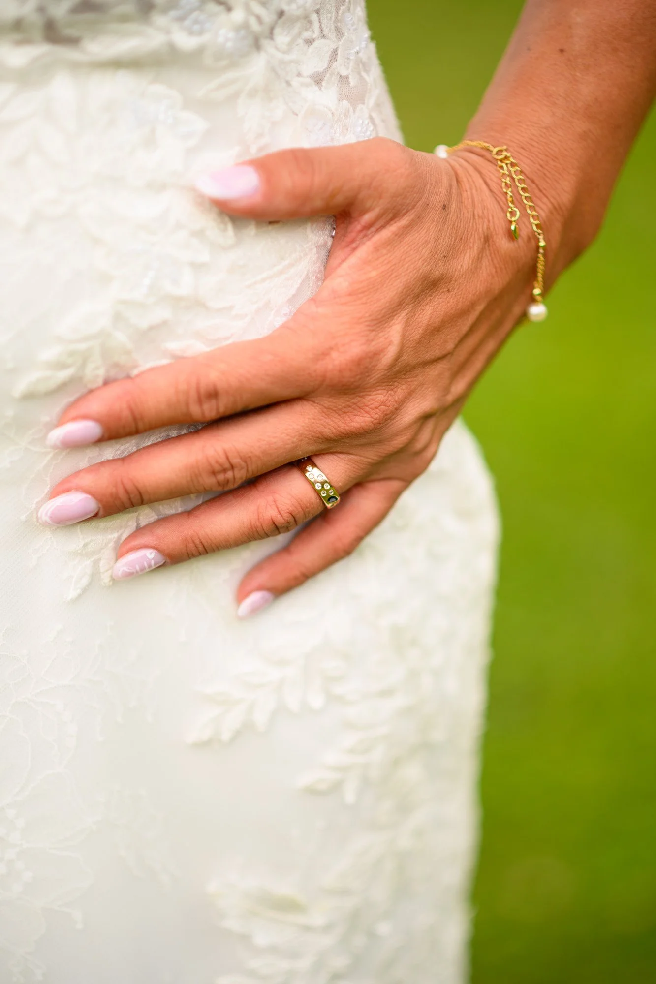 Une main d'une femme portant une robe de mariage, avec une bague en or et des bijoux en or avec des perles.