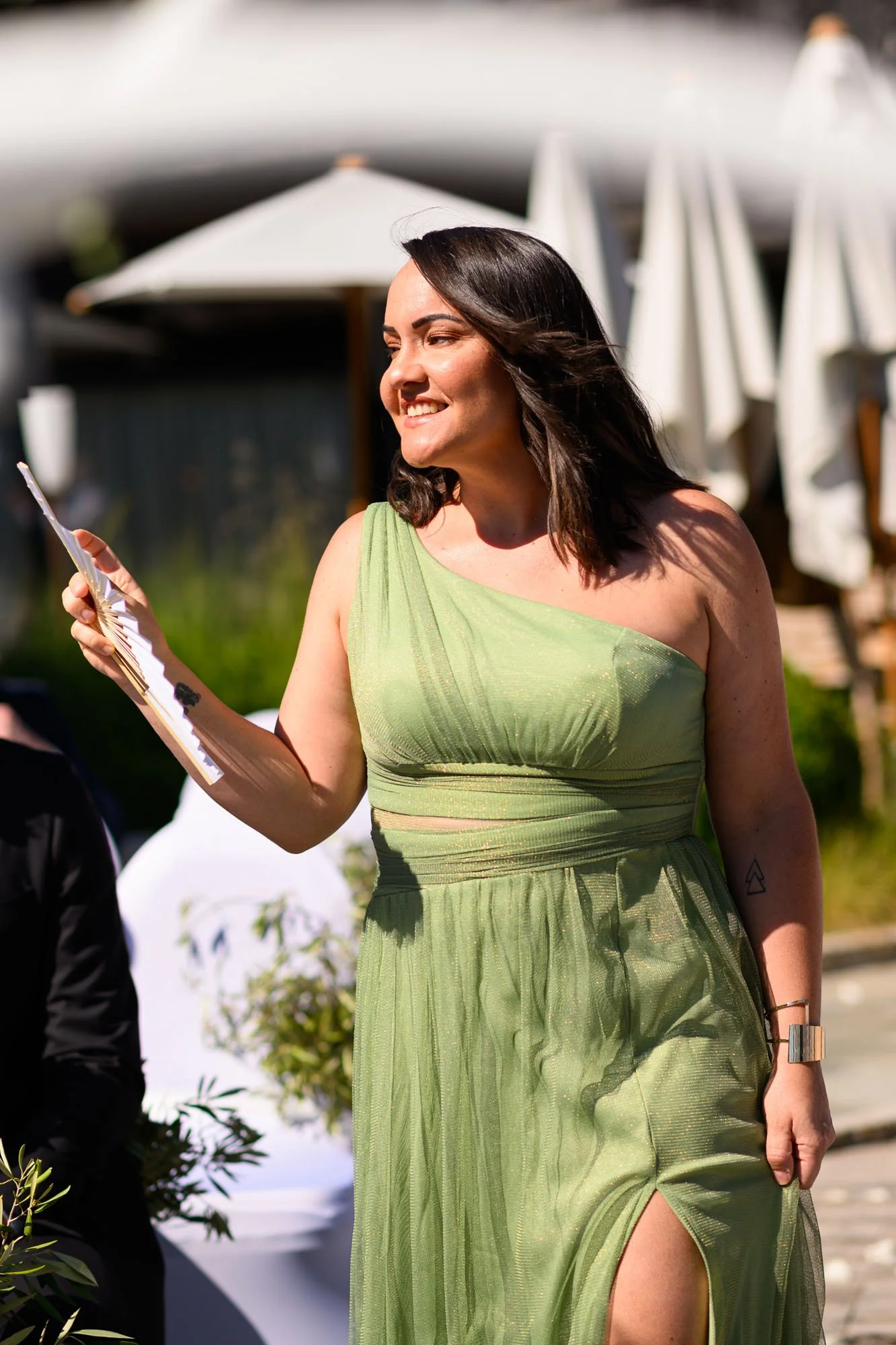 Femme souriante portant une robe verte, tenant un document, en plein air avec des parasols blancs en arrière-plan.