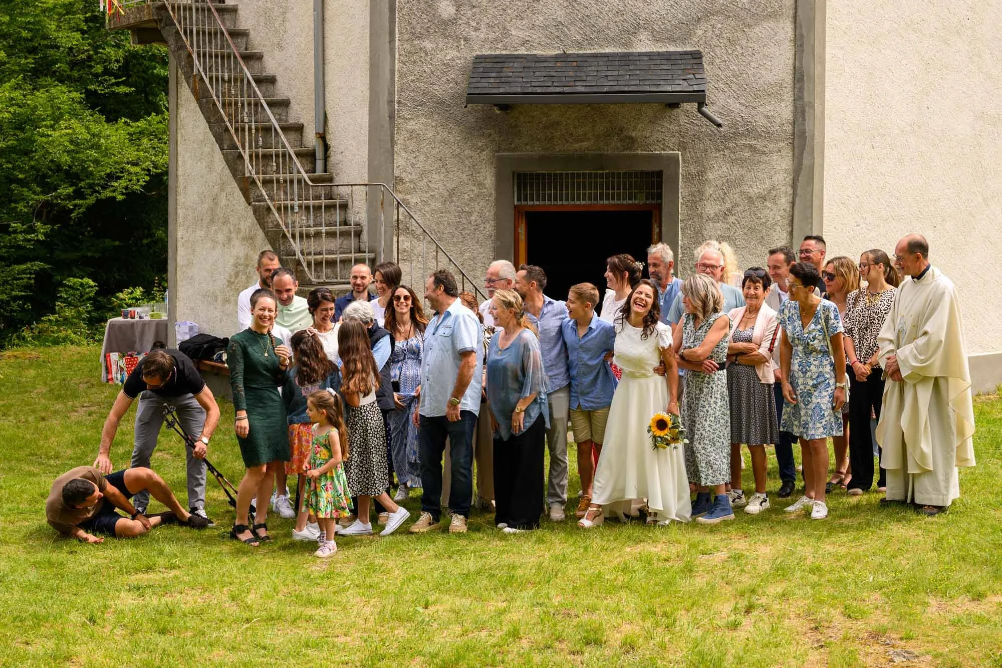 Groupe de personnes posant dehors pour une photo lors d'une occasion spéciale, avec des femmes en robes dehors d'un bâtiment.