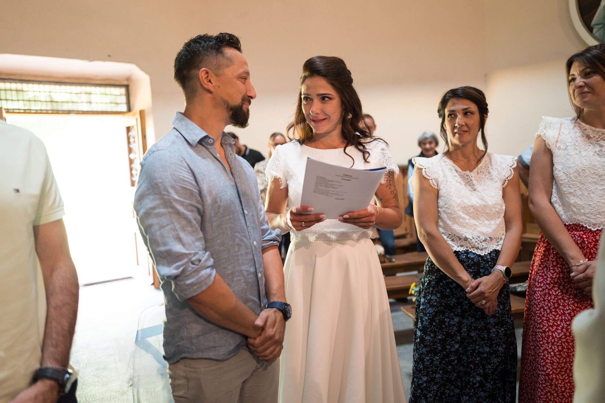 Une cérémonie de mariage en intérieur, un couple échange des vœux, entouré de personnes en attente, ambiance chaleureuse.