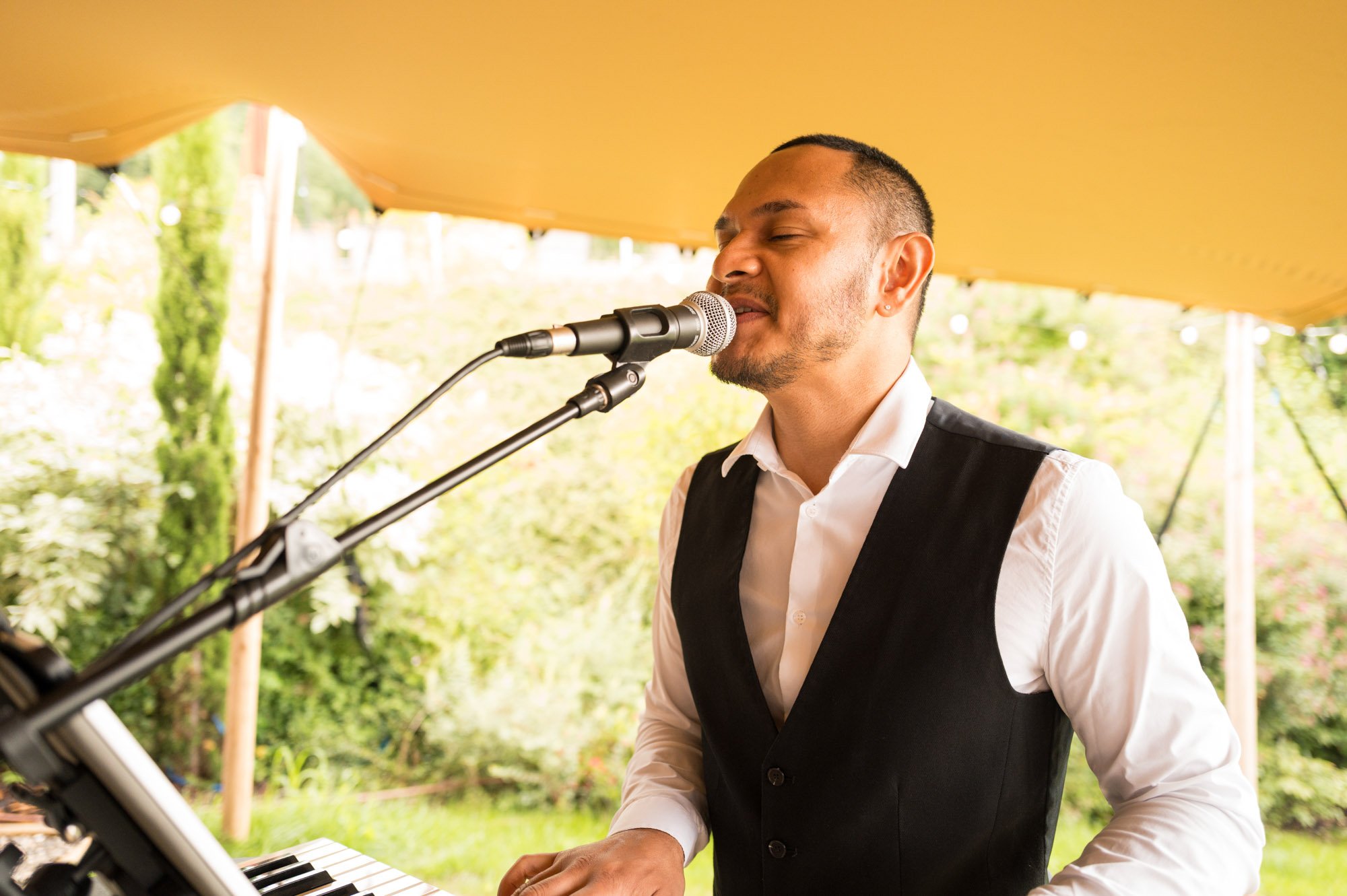 Homme chantant et jouant du clavier sous une tente lors d'un événement en plein air.