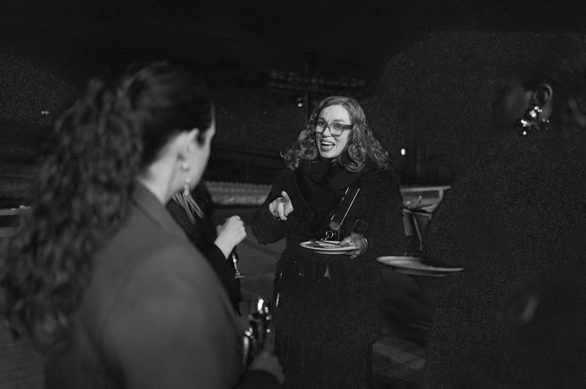Une femme souriante avec des lunettes parle à un groupe de personnes lors d'une conversation dans un environnement intérieur.