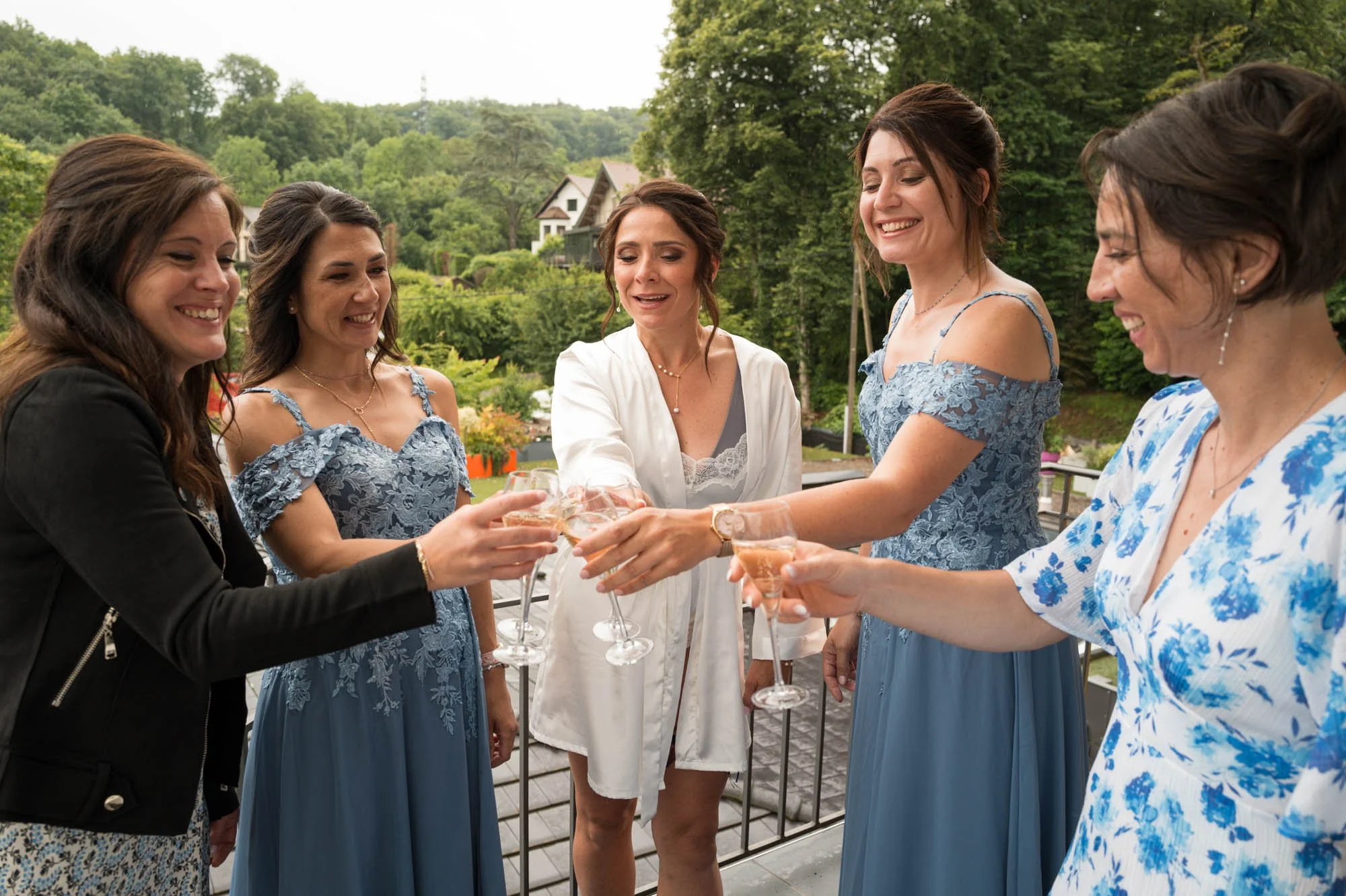 Groupe de femmes souriantes en dress code bleu, célébrant avec des verres de champagne lors d'une occasion en extérieur avec un paysage verdoyant en arrière-plan.