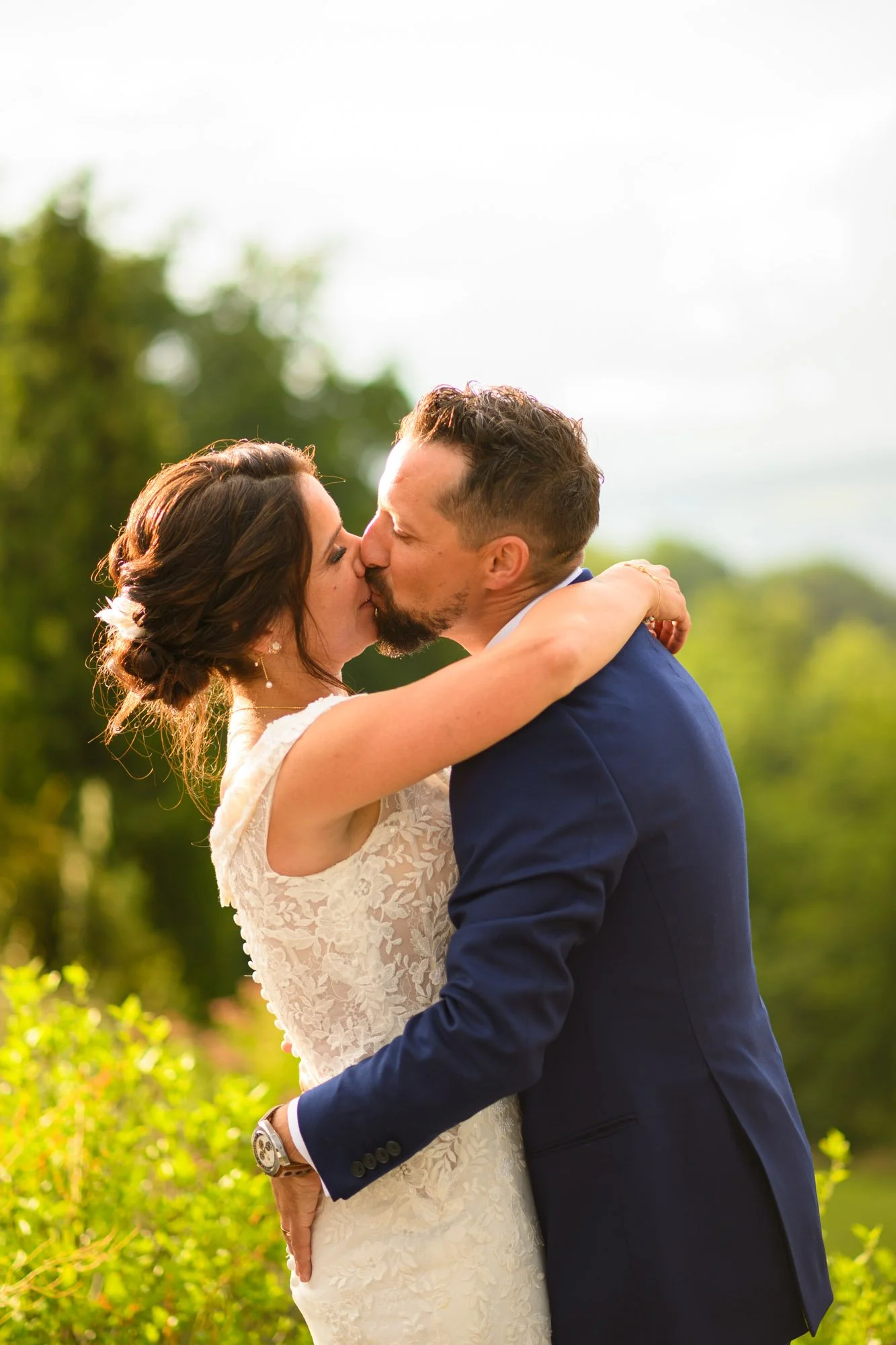Un couple en robe de mariée et costume élégant s'embrassant lors d'un mariage en plein air.