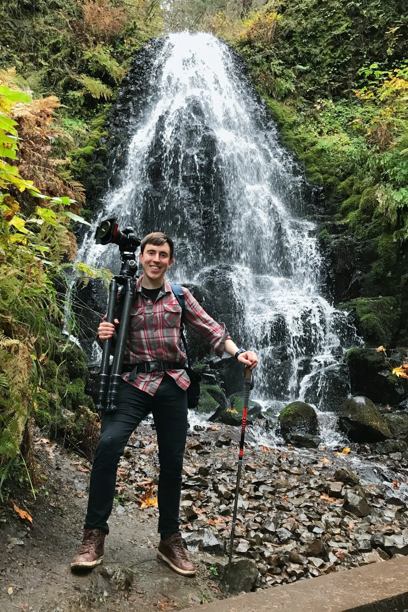 Brendan Alex Phoenix standing with camera gear in front of Fairy Falls in Oregon during autumn 2019.