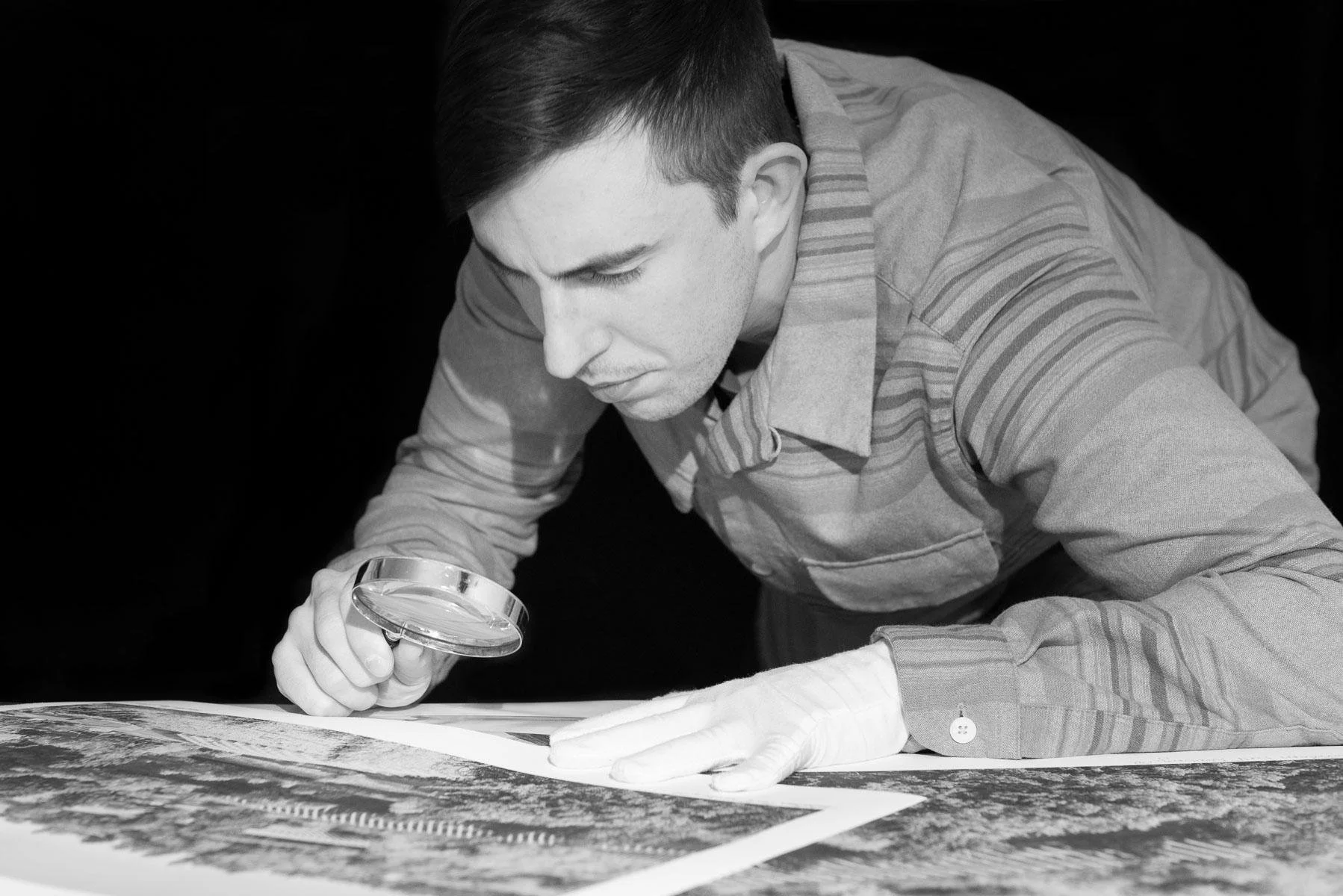 Photographic artist Brendan Alex Phoenix carefully inspecting a fine art print with gloves and magnifying glass, emphasizing attention to detail and authenticity.