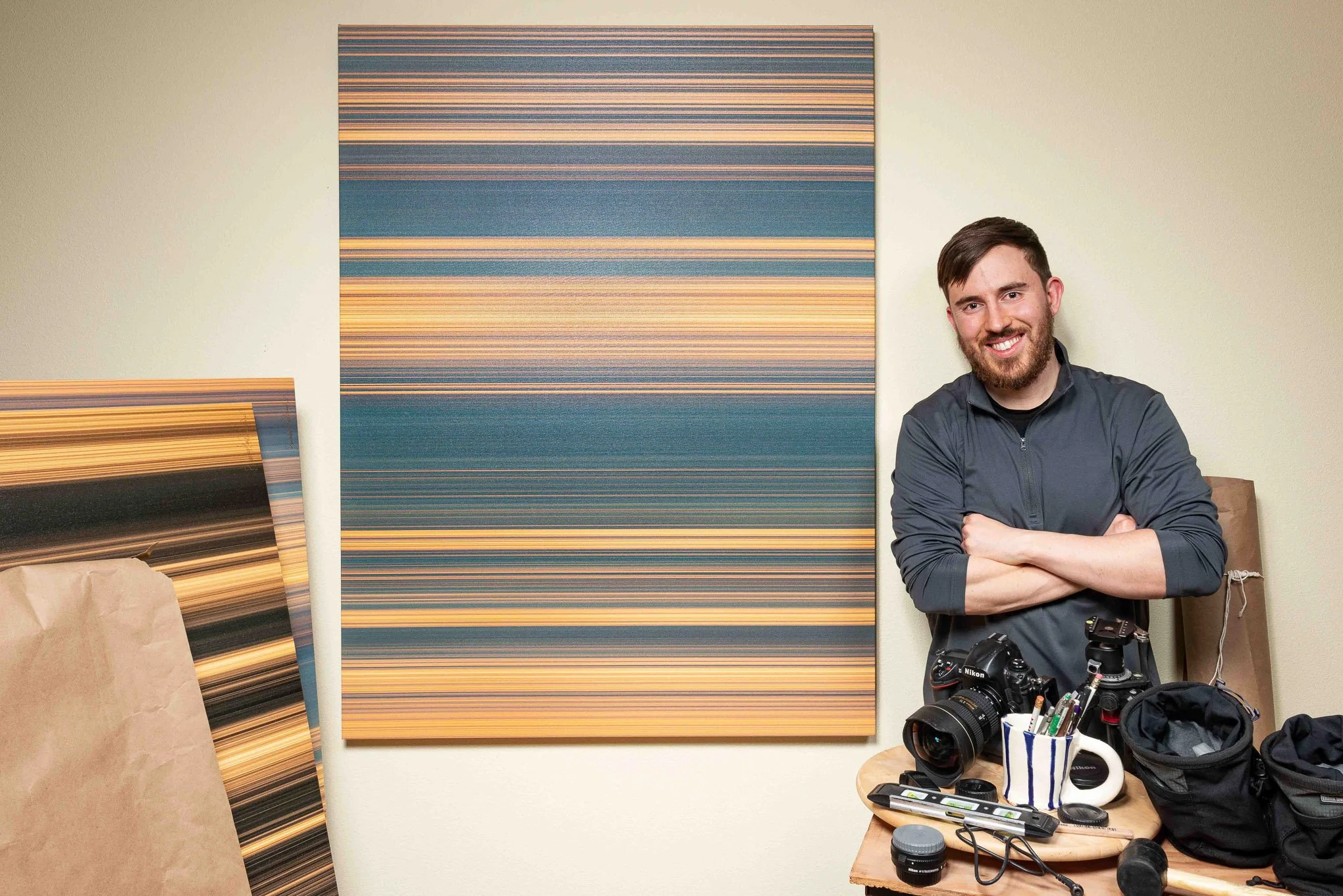 Portrait of Brendan Alex Phoenix standing next to a Stripes BAPstract and camera in his studio.