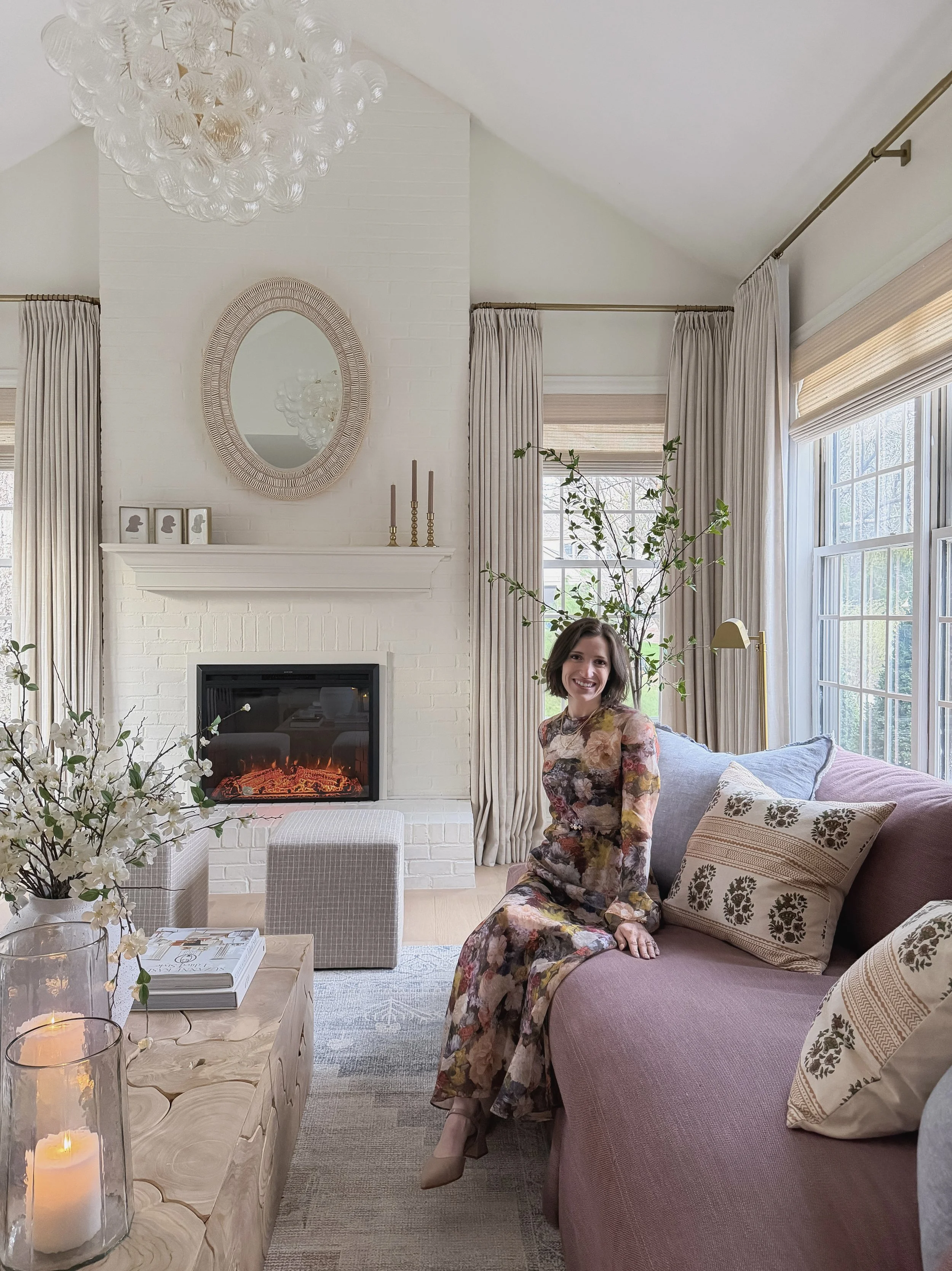 Floor-to-ceiling TwoPages pinch pleat curtains in a bright living room layered over bamboo roman shades