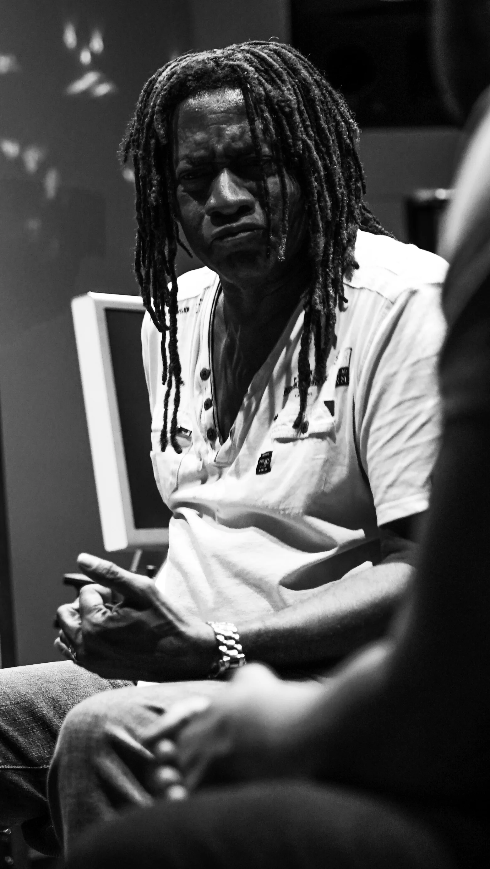 Black-and-white candid portrait of a seated musician with long locs