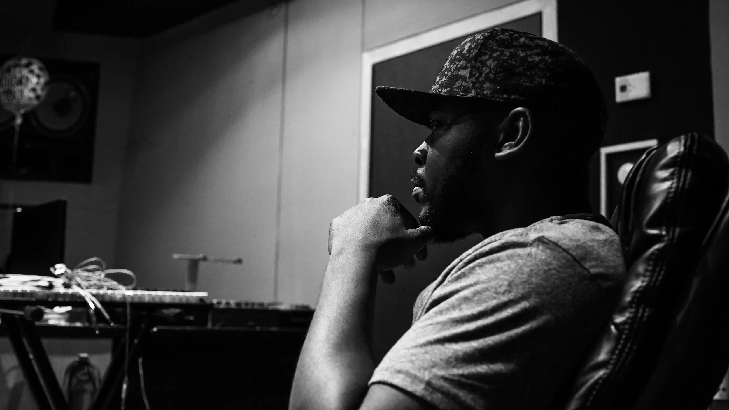 Black-and-white seated musician wearing a cap in a recording studio