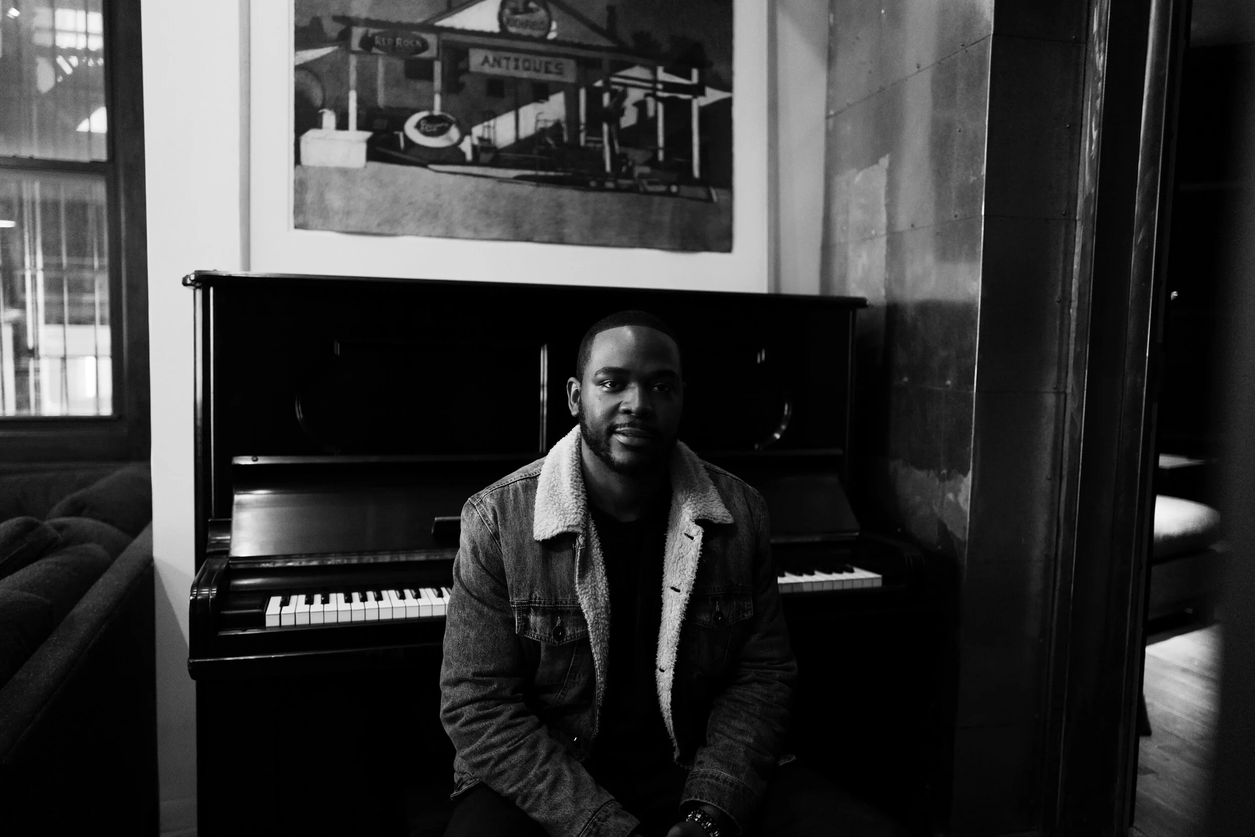 Black-and-white seated portrait beside an upright piano