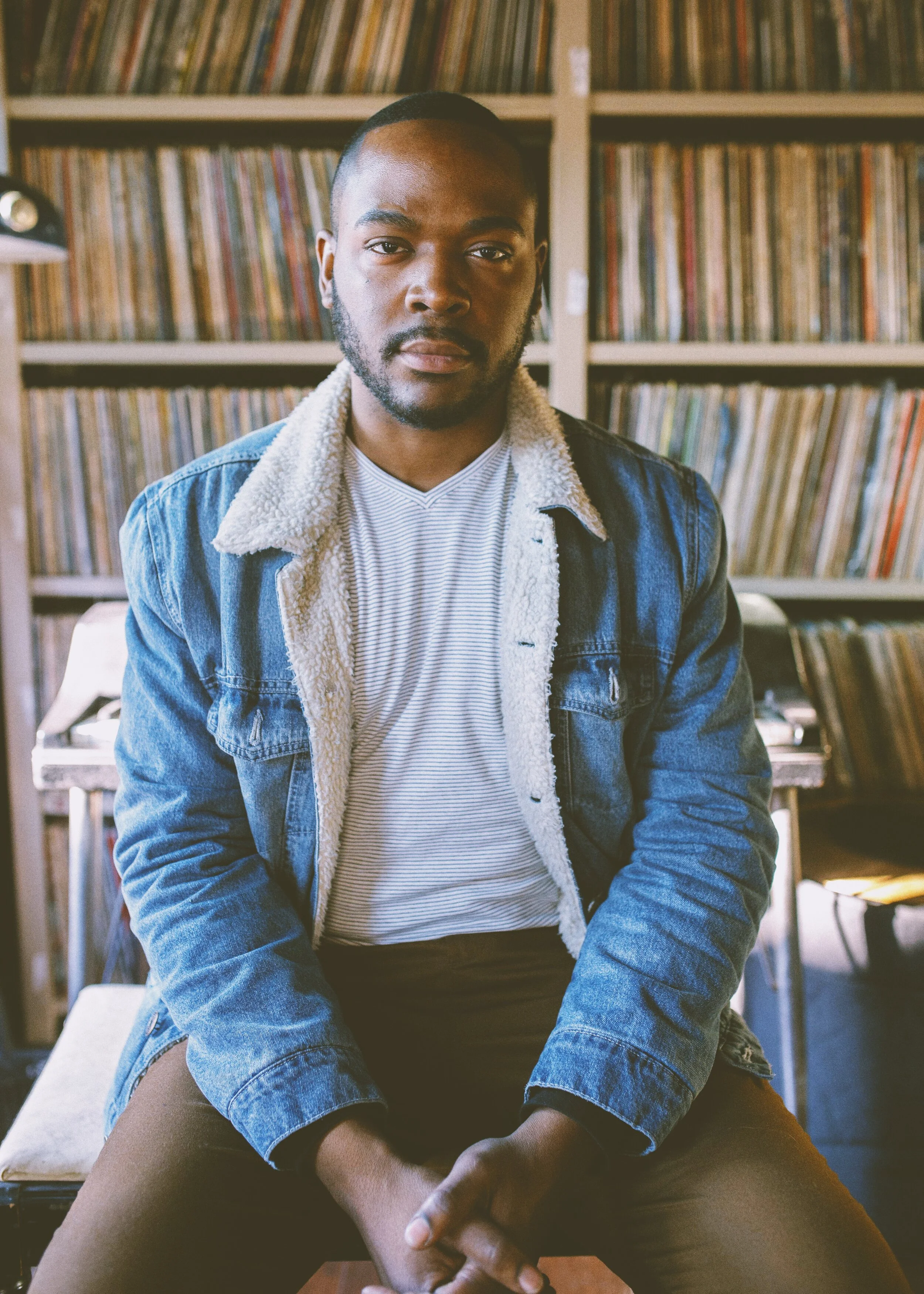 Seated portrait in a denim jacket in front of record shelves