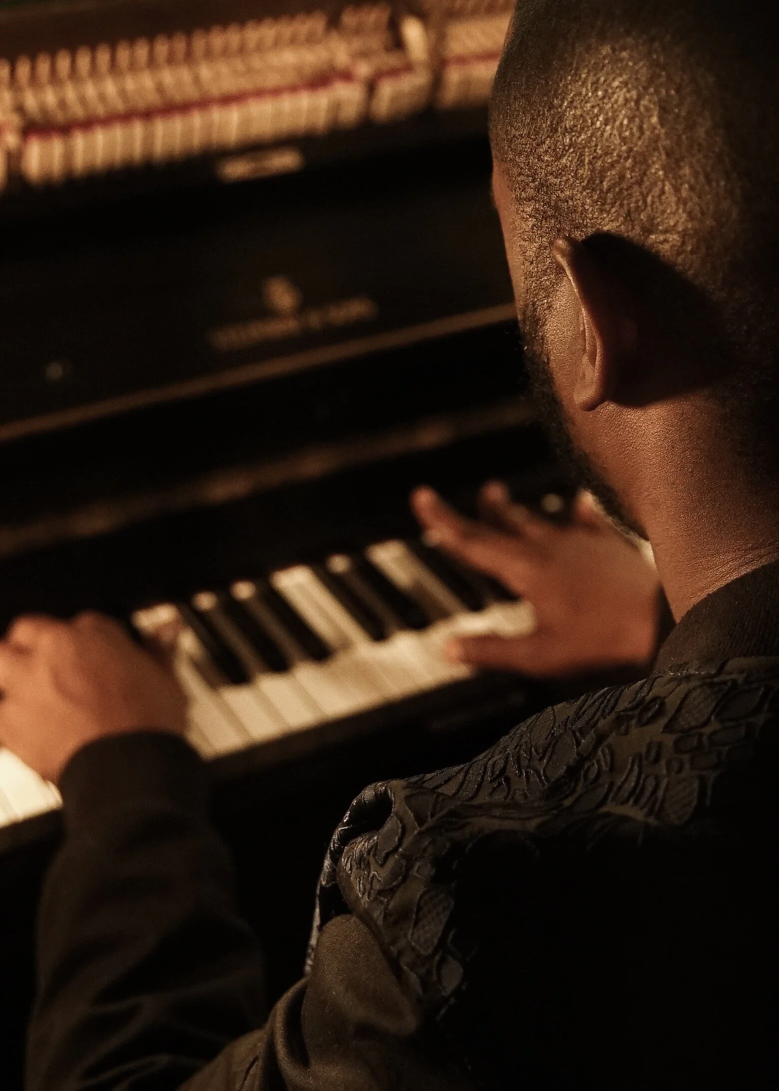 Over-the-shoulder close-up of hands playing an upright piano