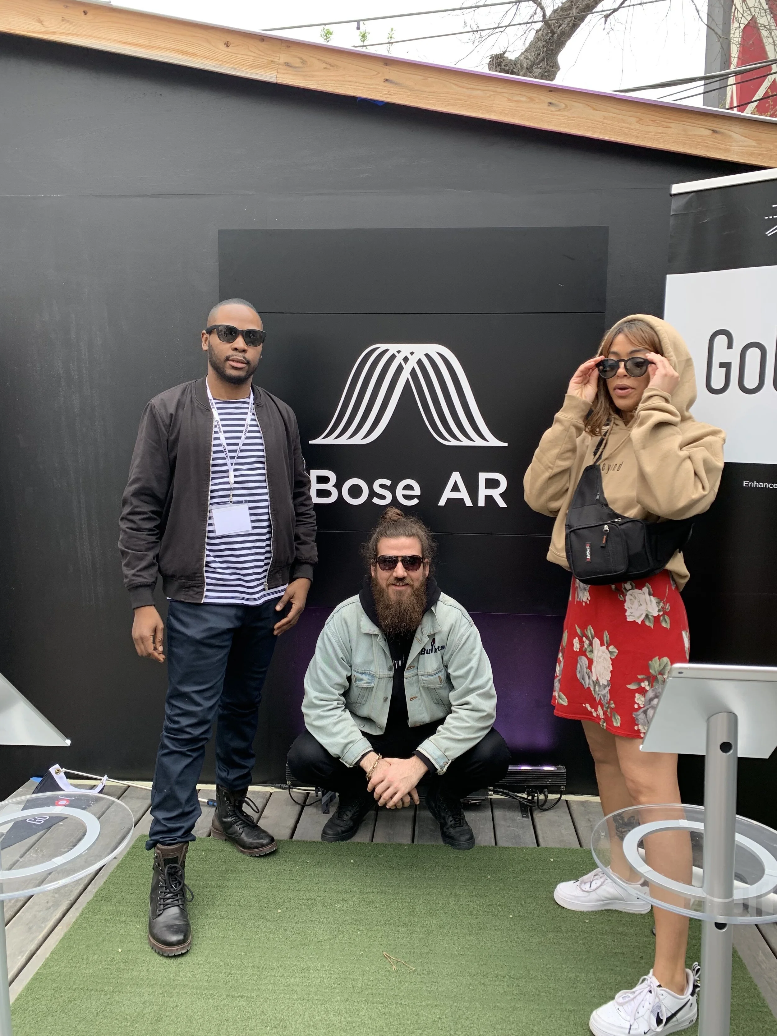 Three people posing beside a Bose AR event display