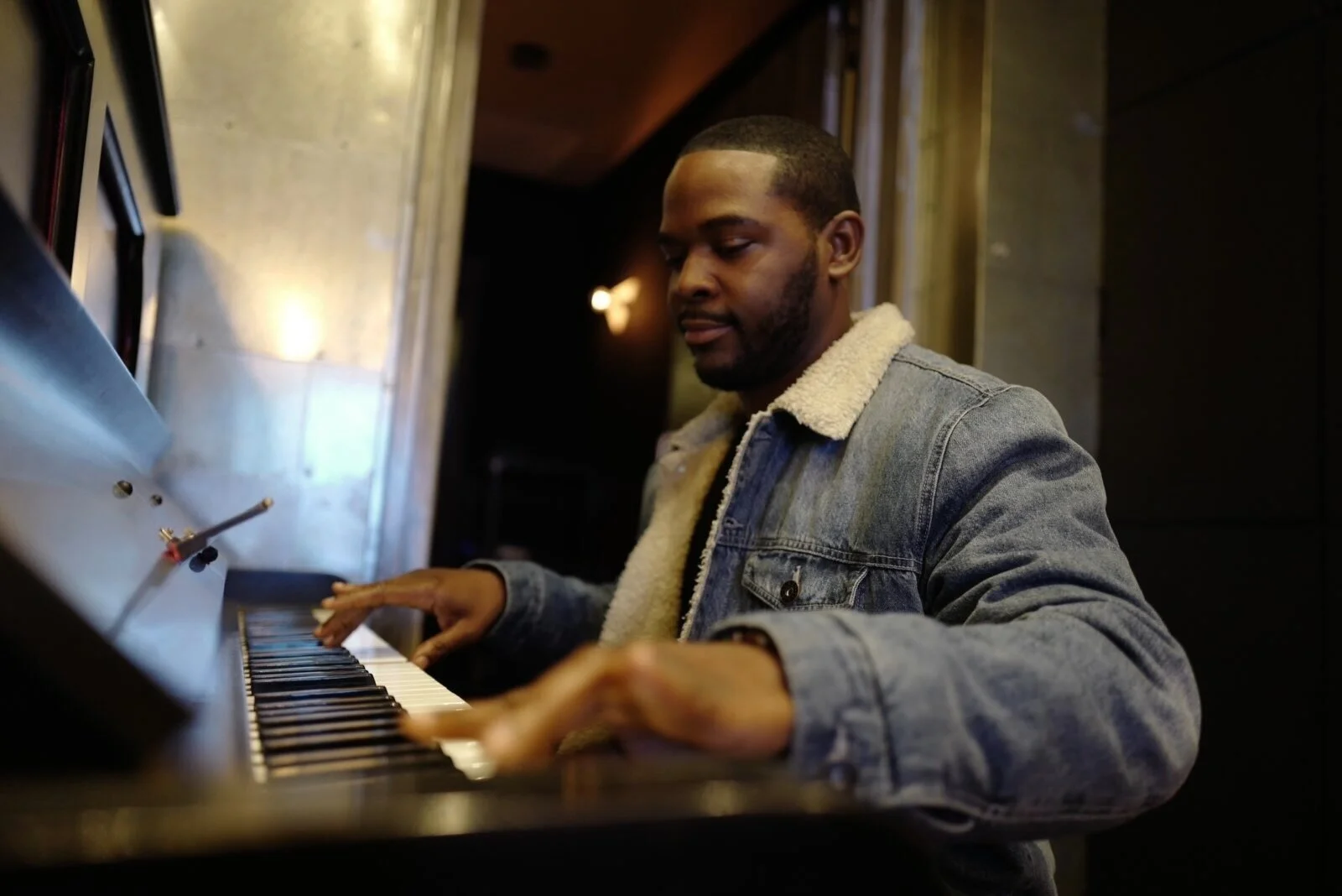 Side view of a pianist in a denim jacket playing an upright piano