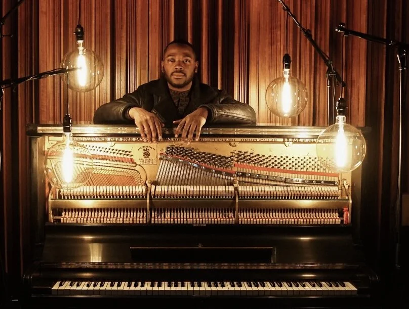 Portrait leaning over an open upright piano beneath hanging lights