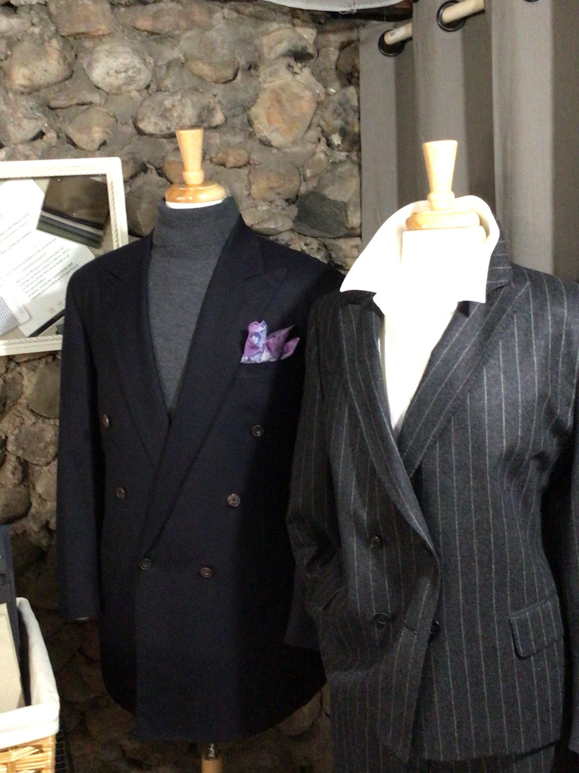 Navy double-breasted jacket and gray chalk-stripe suit displayed on mannequins.