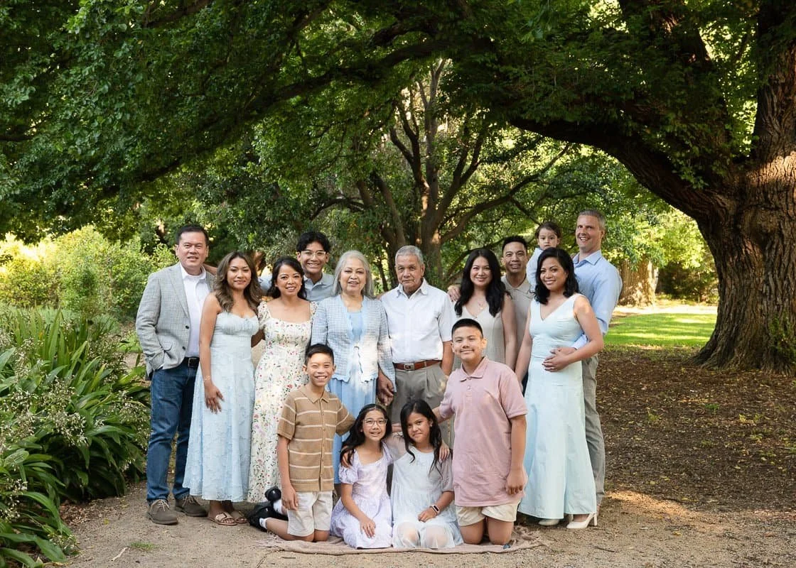 Outdoor photo of a large extended family standing under a big tree