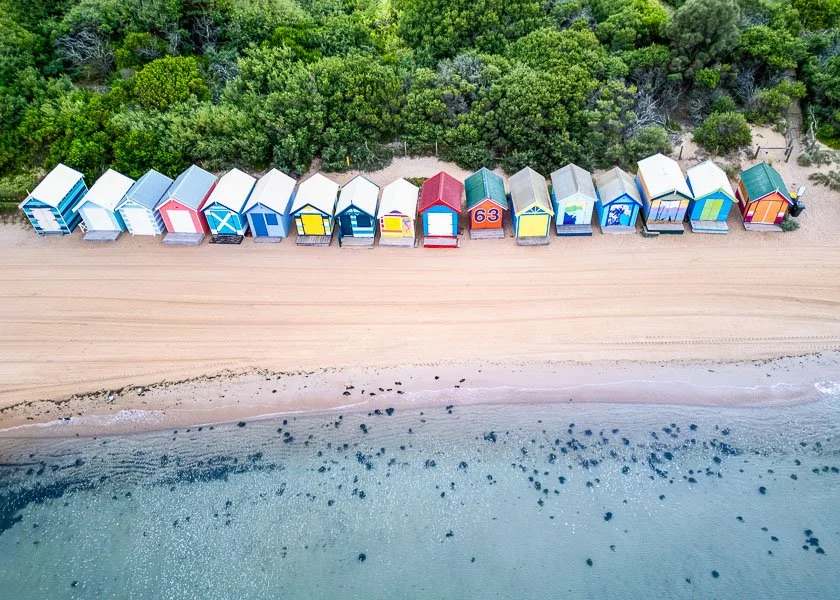 Susan Bradfield Photography images of the  Bayside Brighton beach boxes in Melbourne, Australia. The image is taken from above looking down at the water, boxes and the foliage.